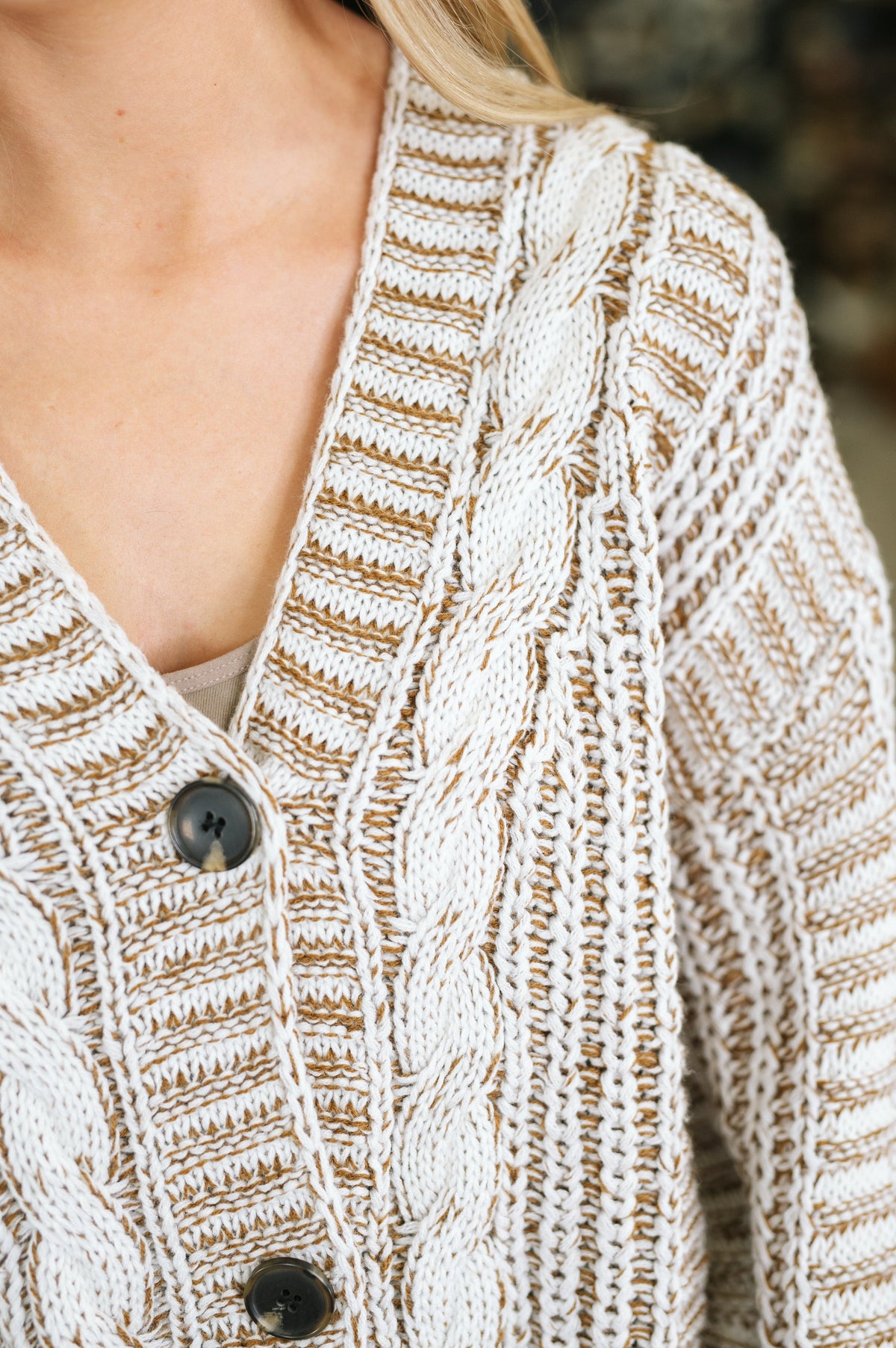 Close-up of a woman wearing a beige cable knit cardigan with a deep V neckline textured stitching and dark front buttons
