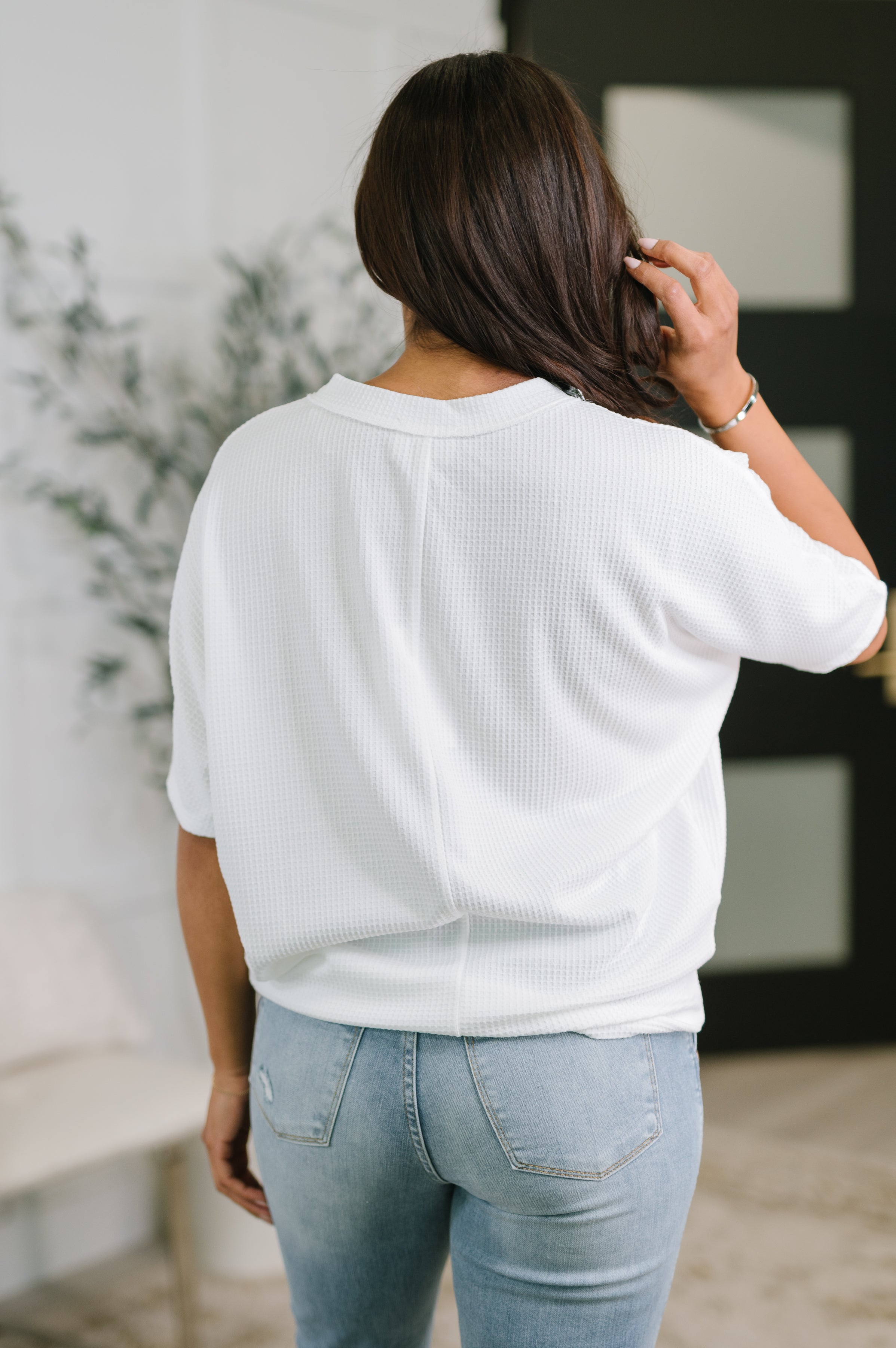 Back view of woman wearing an ivory textured V-neck tee paired with light blue jeans in a casual indoor space