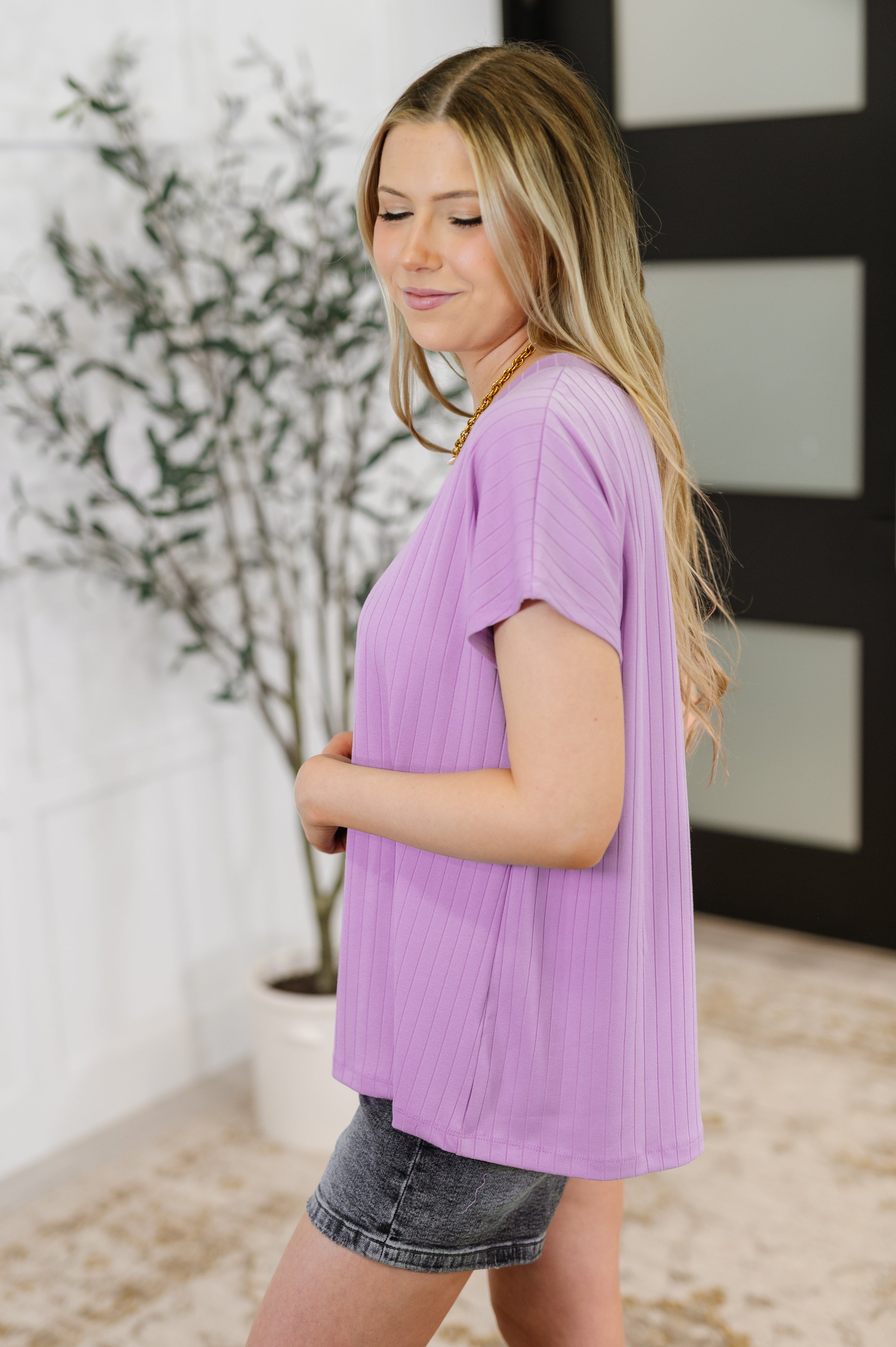 Woman wearing a relaxed fit lavender ribbed short sleeve top paired with faded black denim shorts
