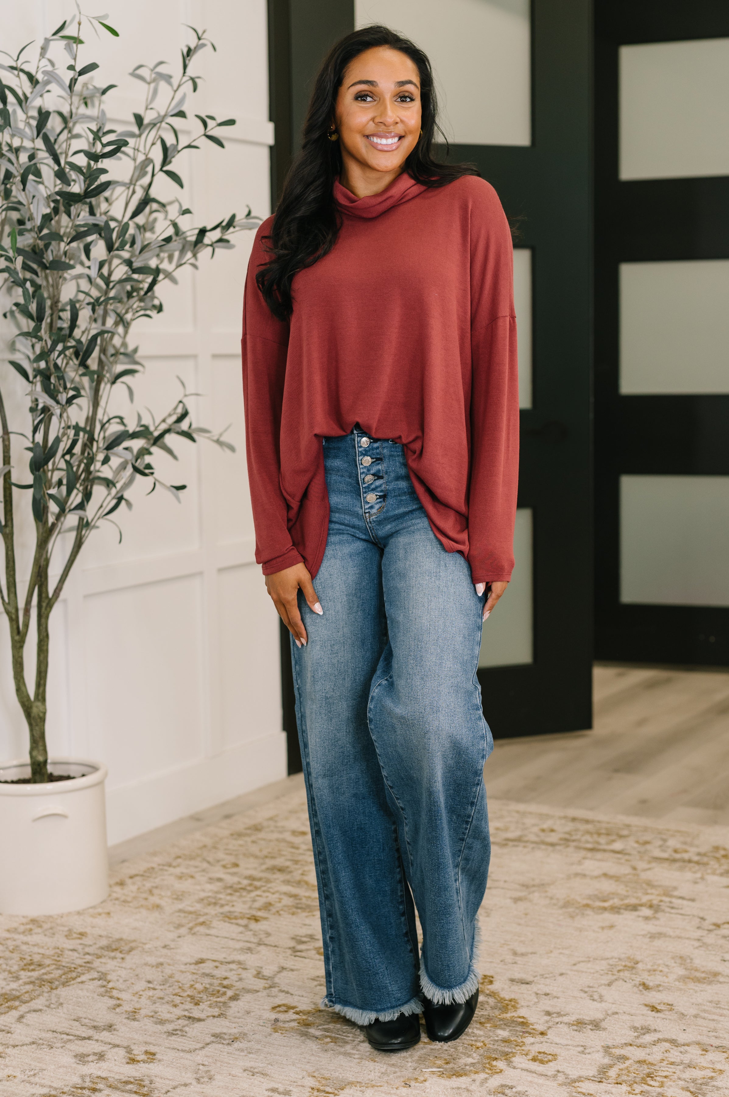 Woman wearing a loose wine-colored cowl neck pullover paired with high-waisted wide-leg jeans indoors