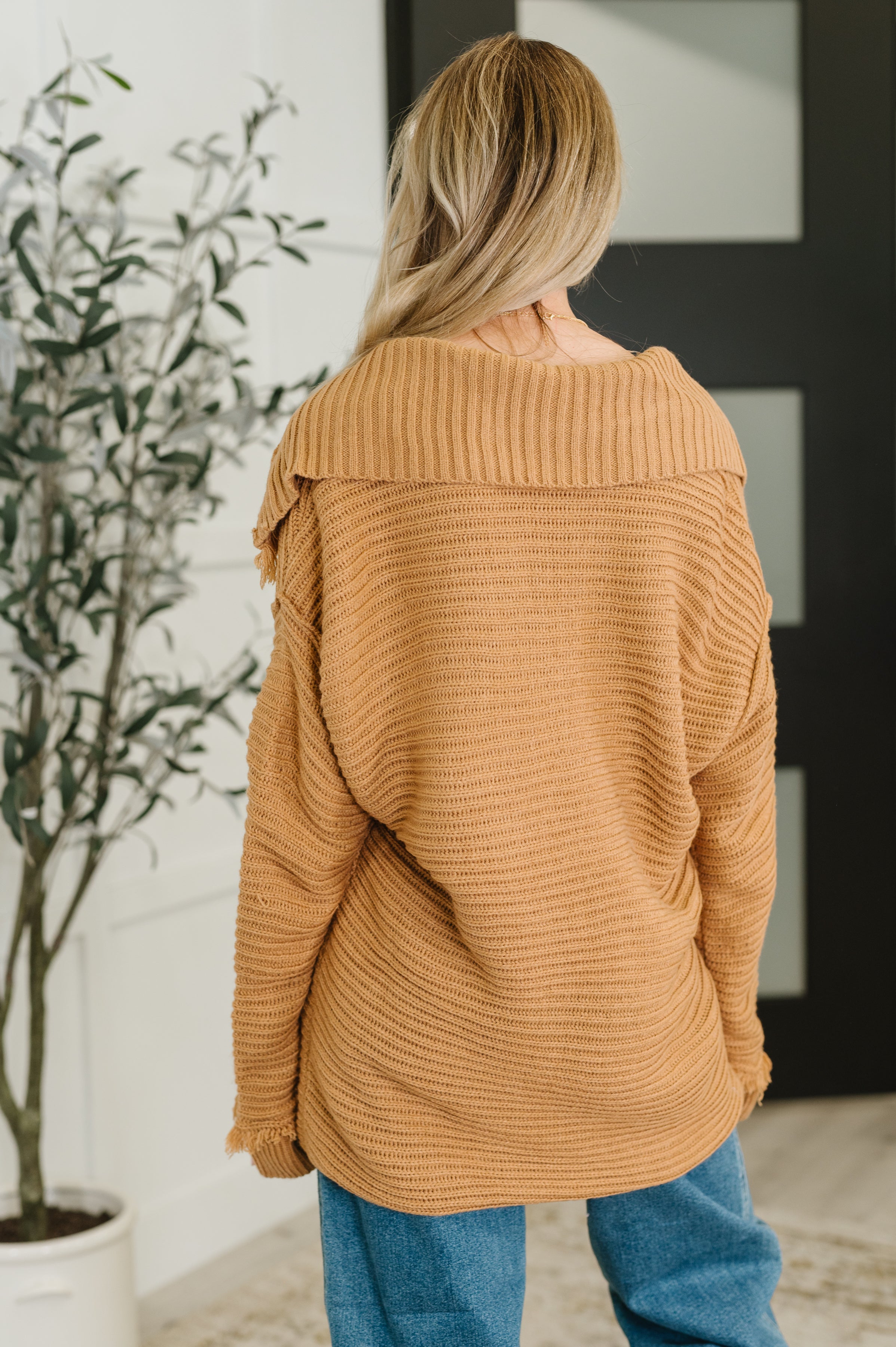 Woman wearing a camel oversized knit sweater with wide collar paired with relaxed blue jeans indoors