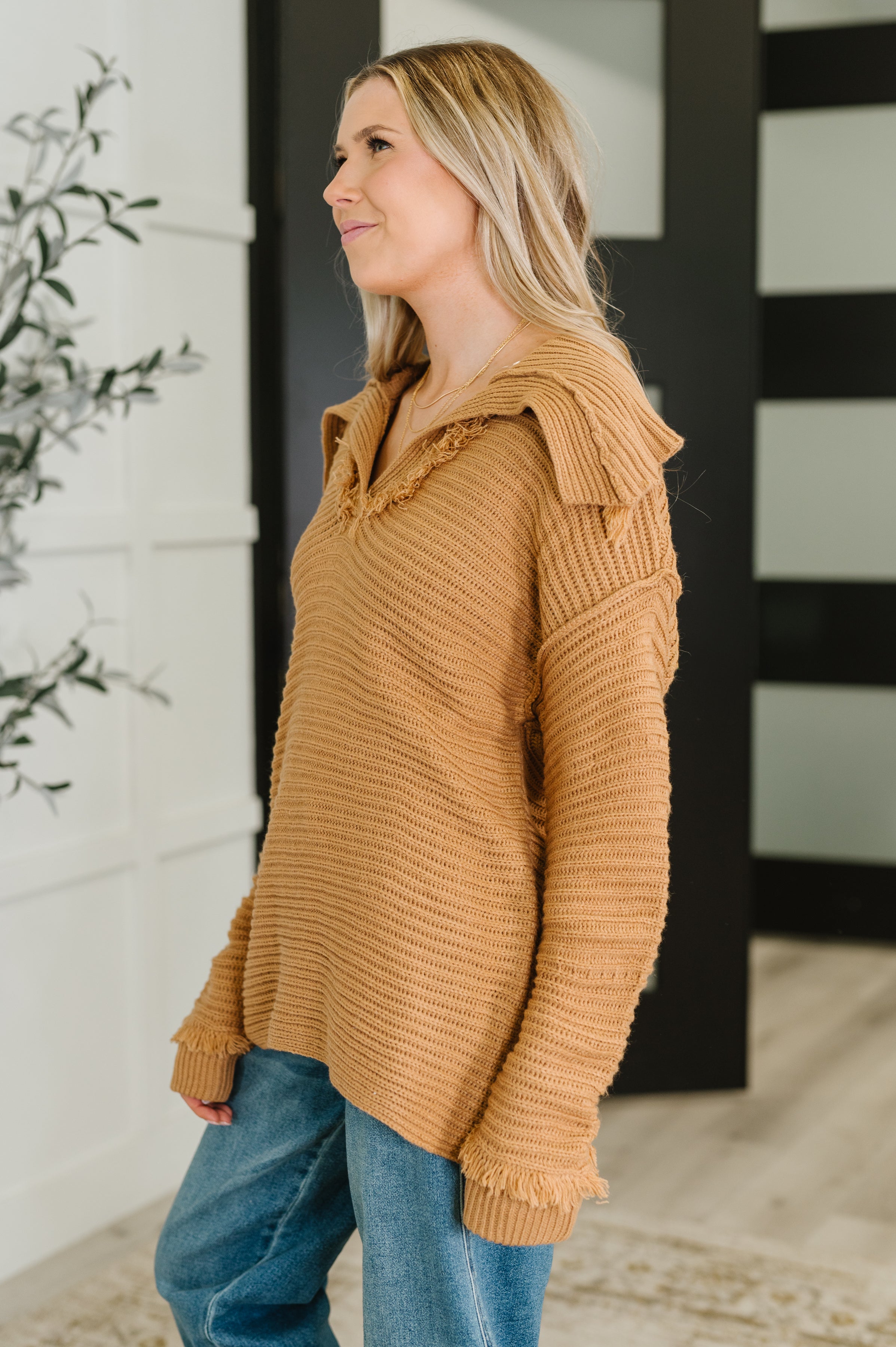 Woman wearing a camel-colored textured sweater with a wide collar paired with relaxed blue jeans indoors