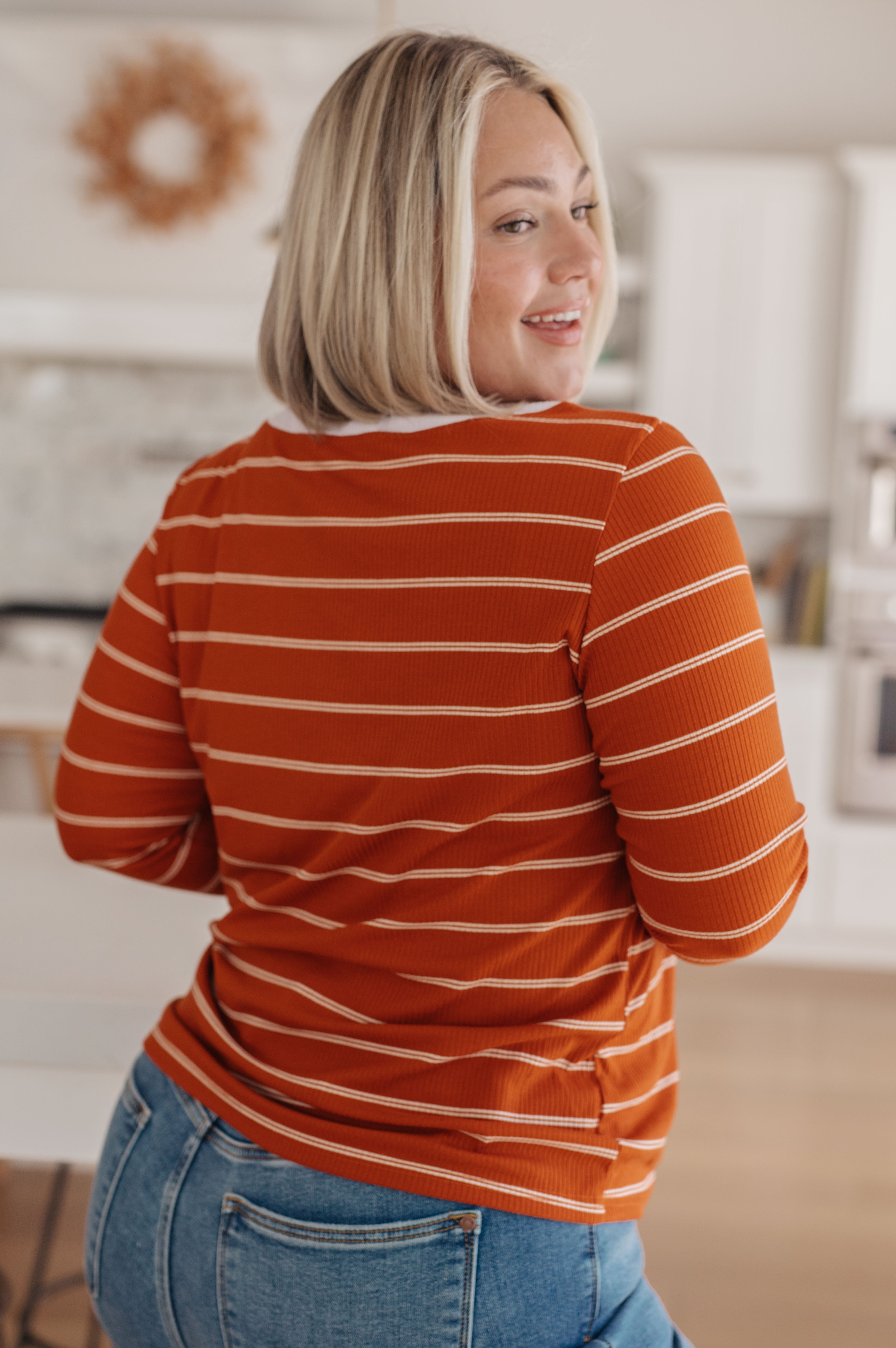 Woman wearing an orange striped long sleeve top with blue jeans in a bright casual indoor space