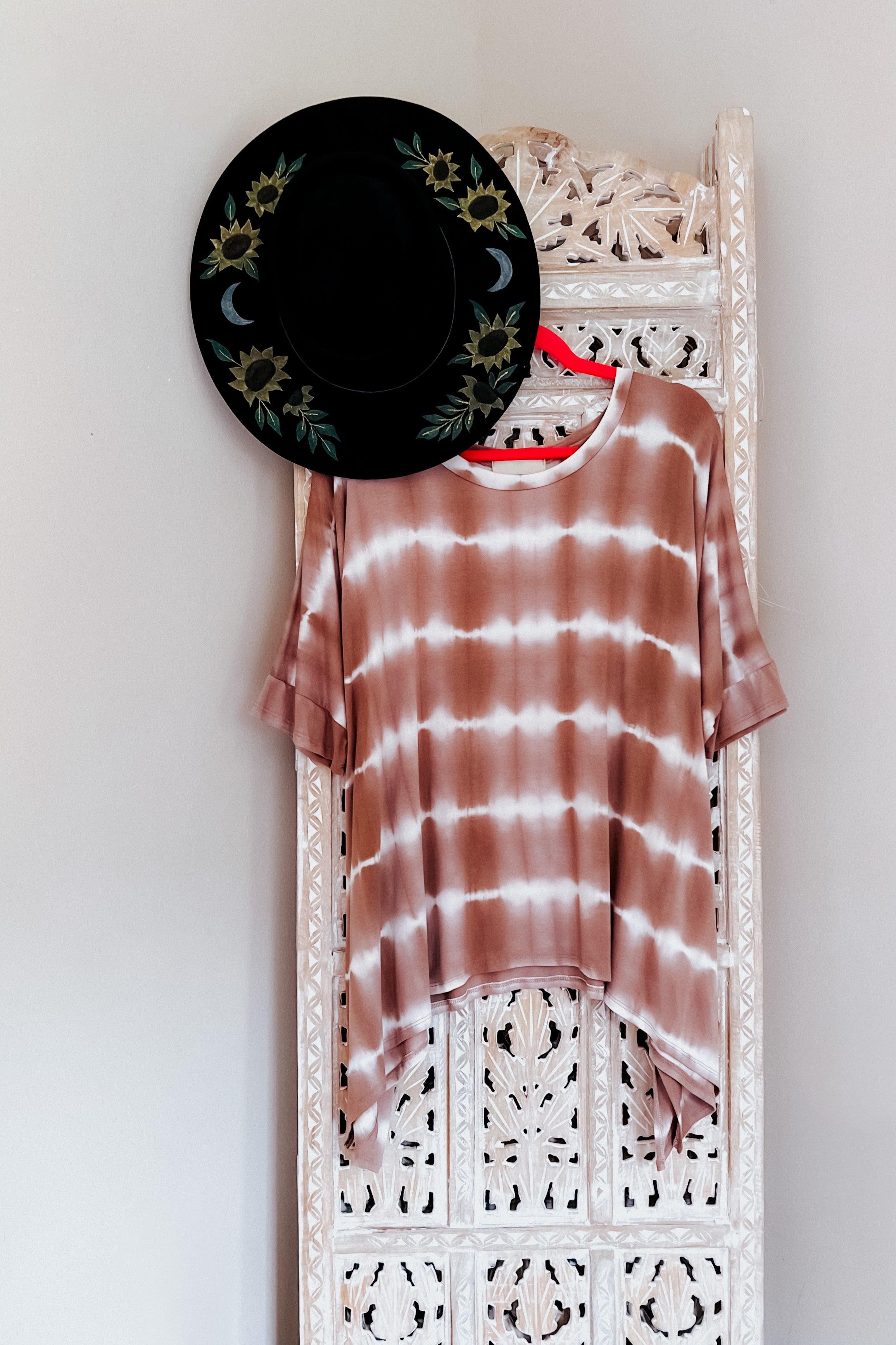 Pink and white striped tie dye tunic hanging on a carved wooden screen with a black floral wide brim hat