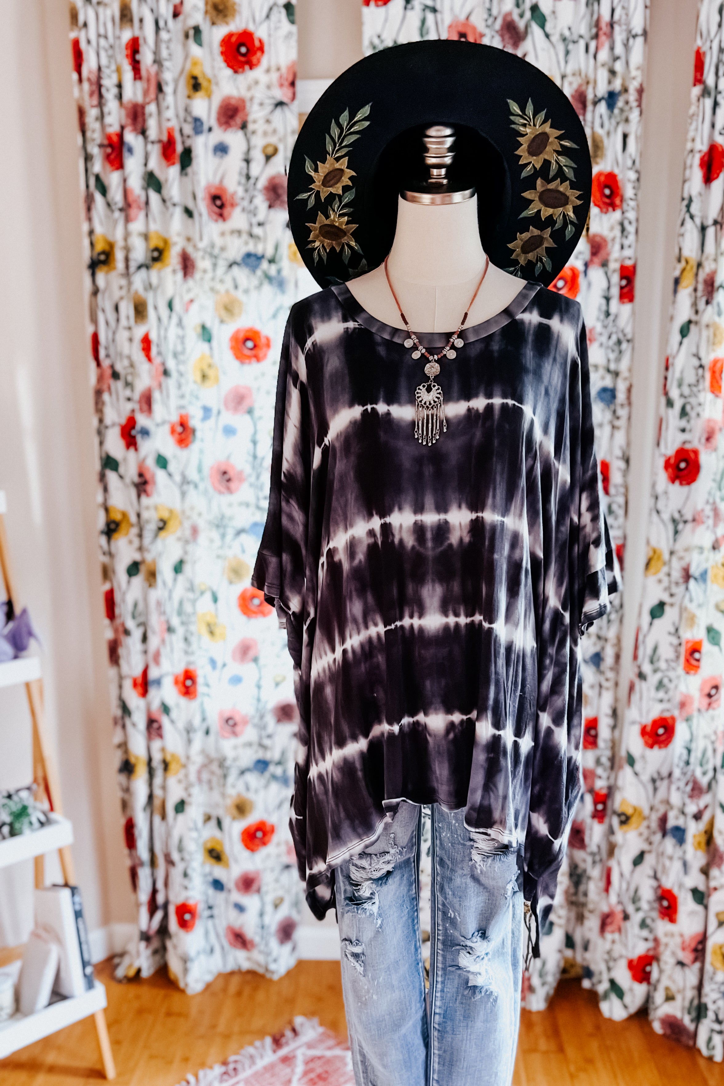 Black and white striped tie dye tunic styled with layered necklaces, paired with distressed denim jeans and a wide-brimmed hat.