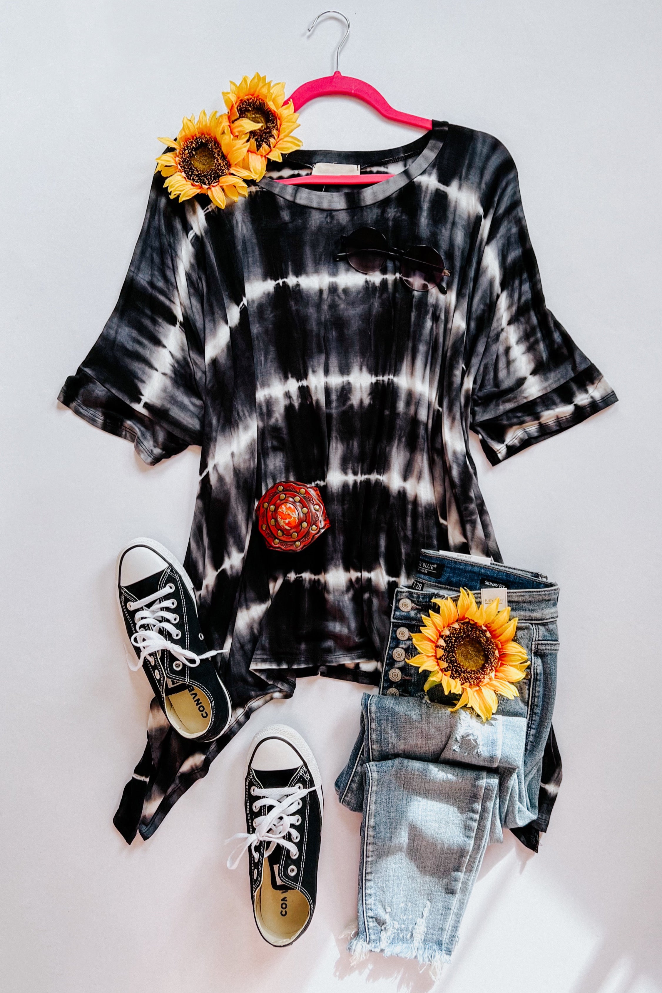 Black and white striped tie dye tunic styled with distressed jeans, black sneakers, sunglasses, and sunflower accents