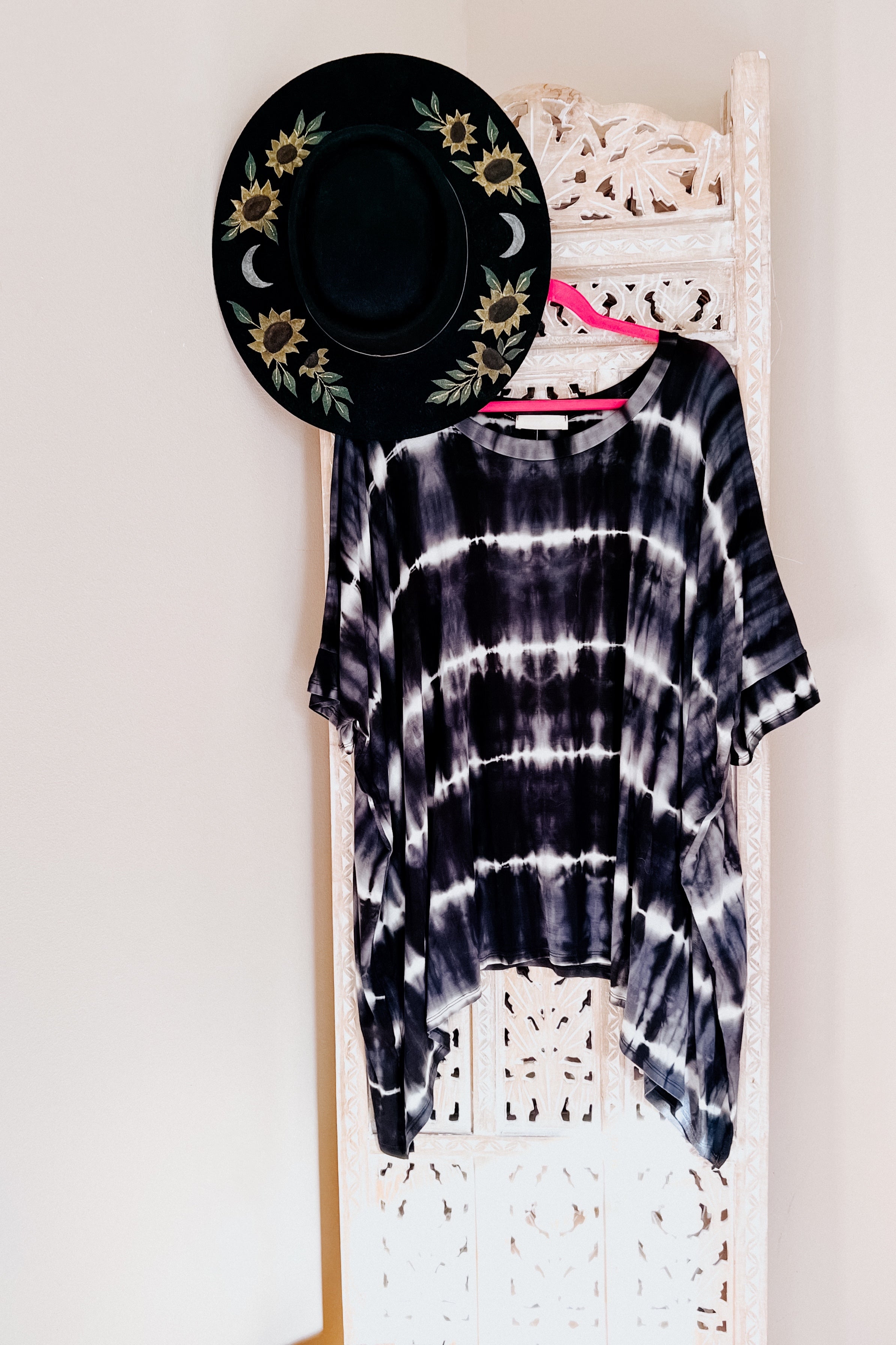 Black and white striped tie dye tunic hanging on a pink hanger with a black sunflower embroidered hat above