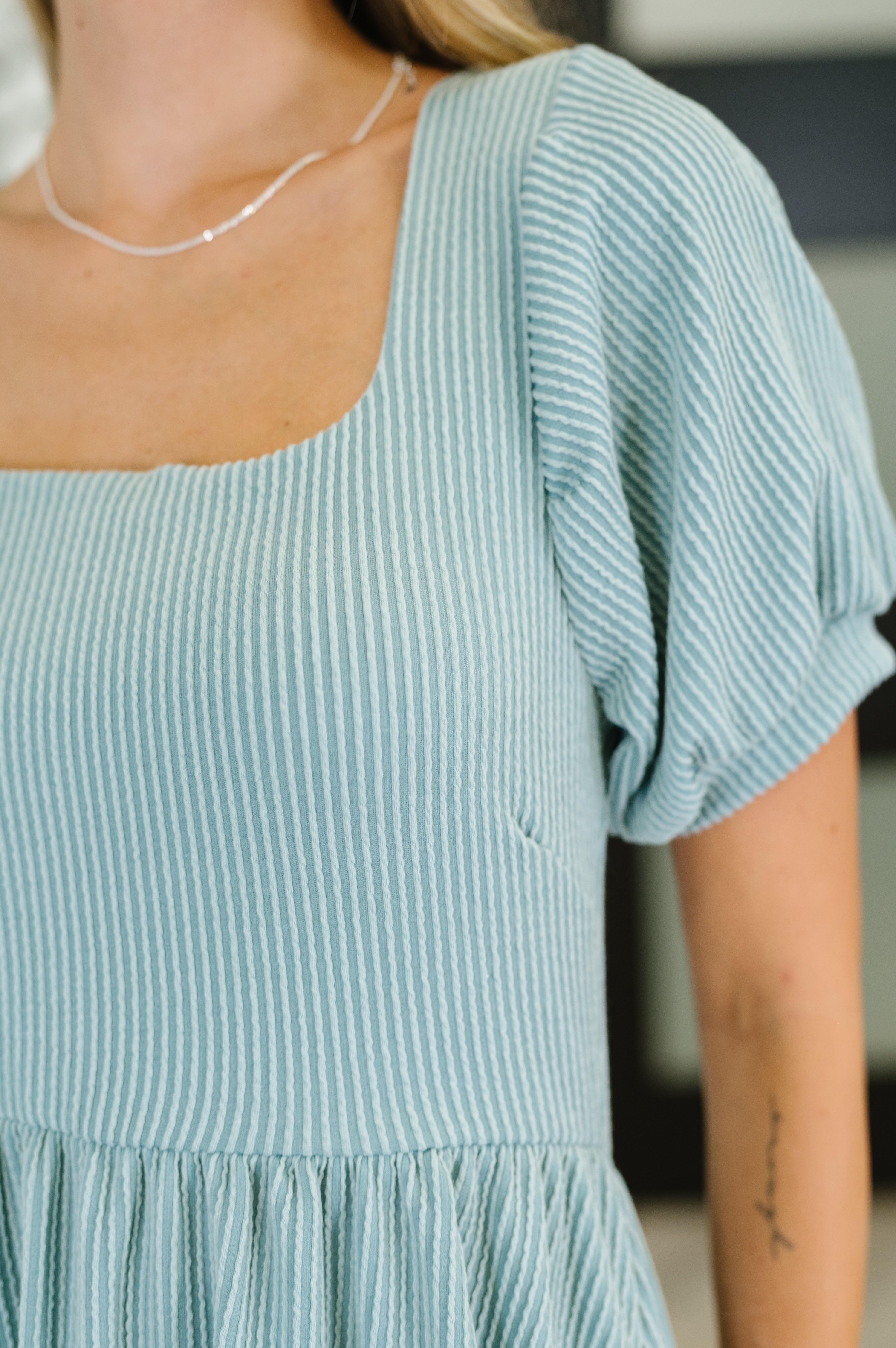 Close-up of a light sage ribbed knit dress with puff sleeves and square neckline on a person wearing a delicate chain necklace
