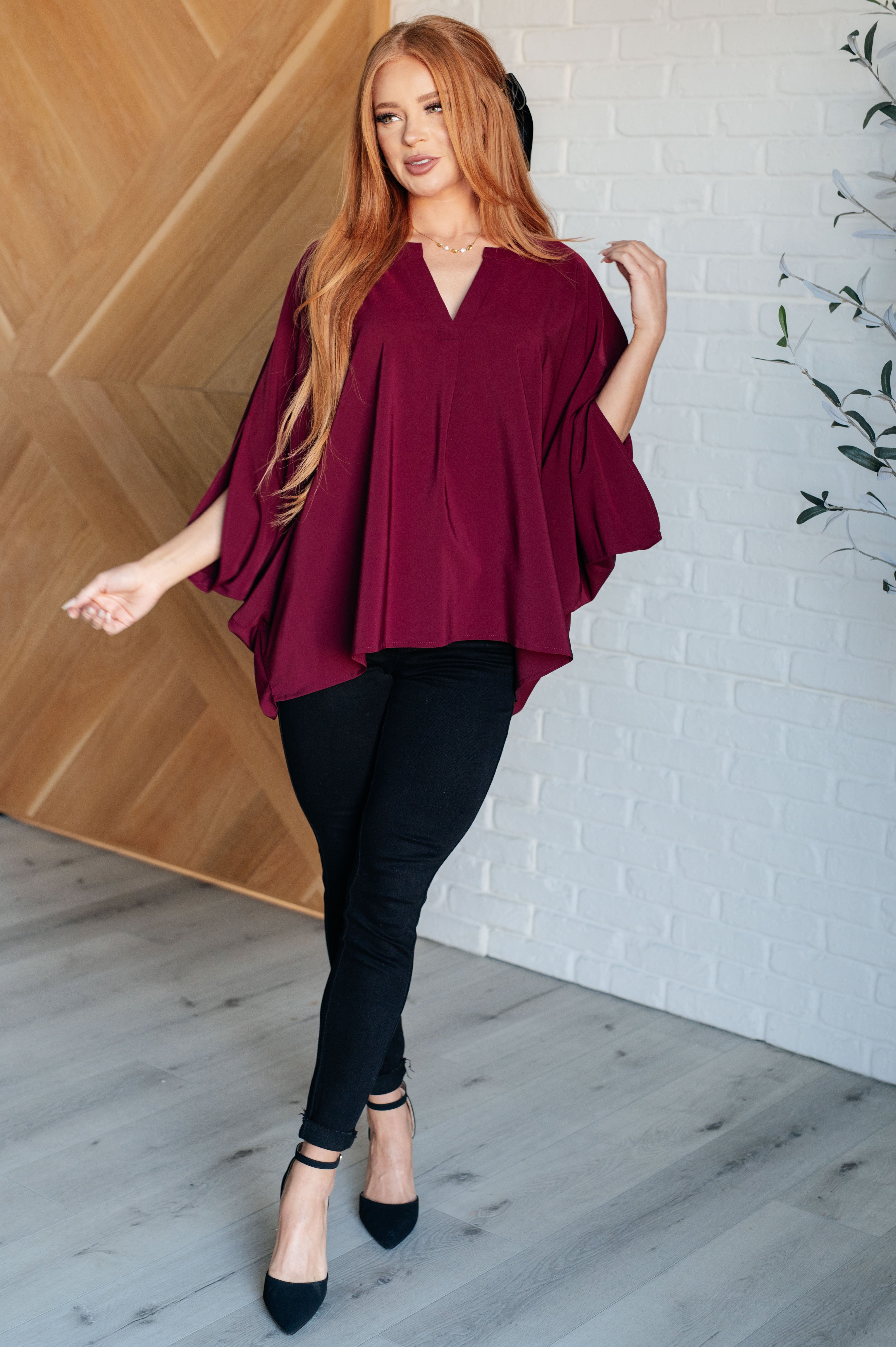 Woman wearing a loose wine-colored blouse paired with black skinny pants and heels in a bright modern room