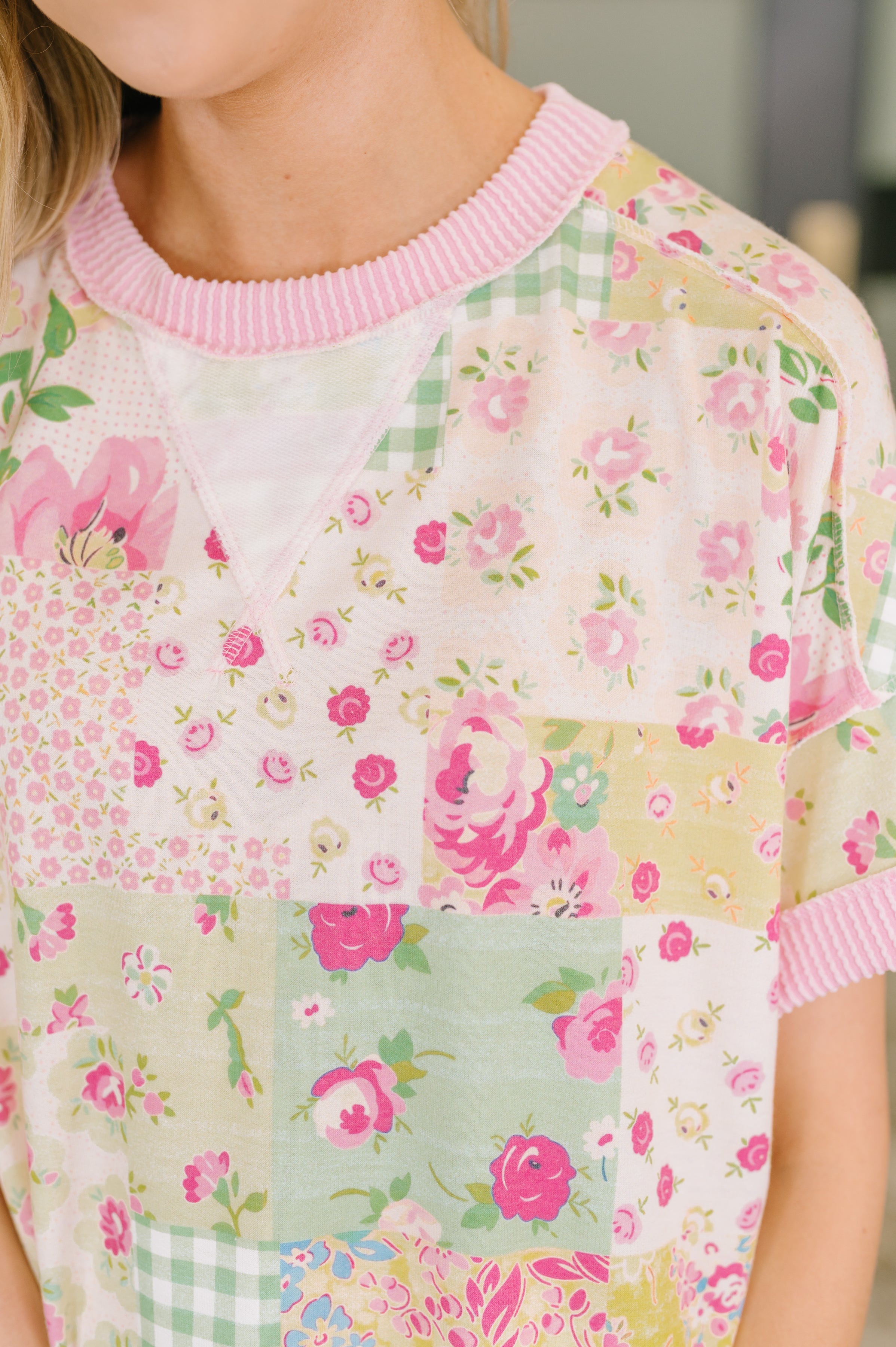 Close-up of pink patchwork tee with floral and gingham patterns, featuring cable ribbed knit neckline in eclectic style