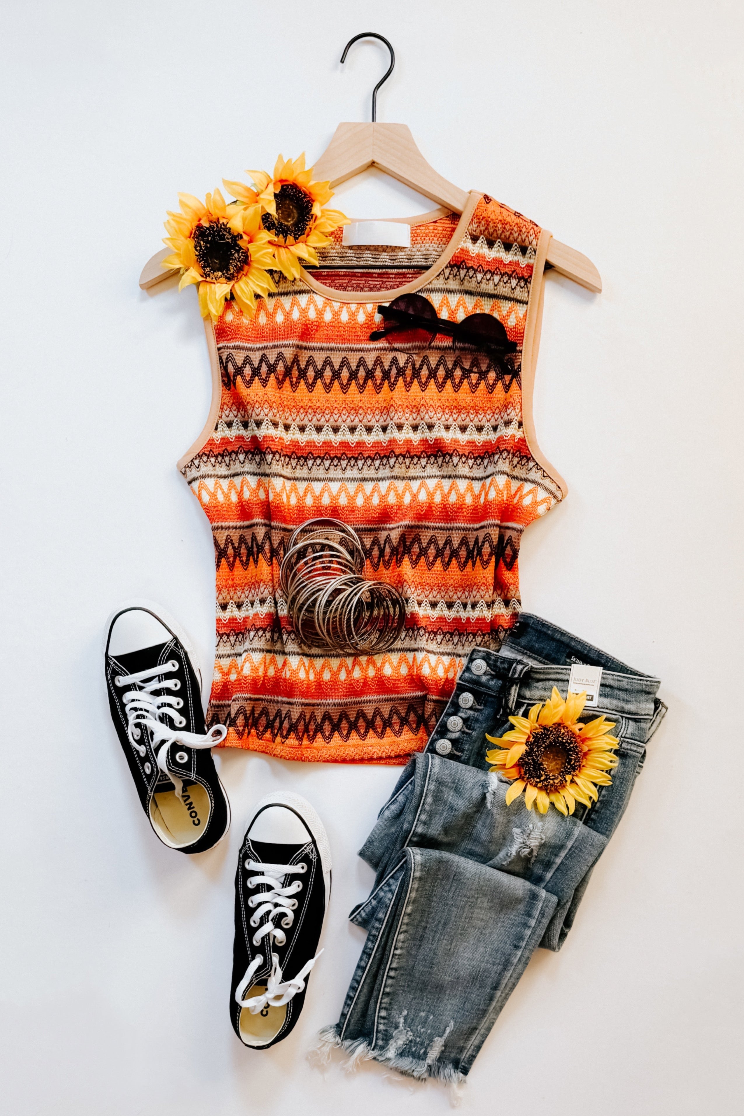 Orange knit tank with bold patterns styled with black sneakers, distressed jeans, sunglasses, bangles, and sunflower accents