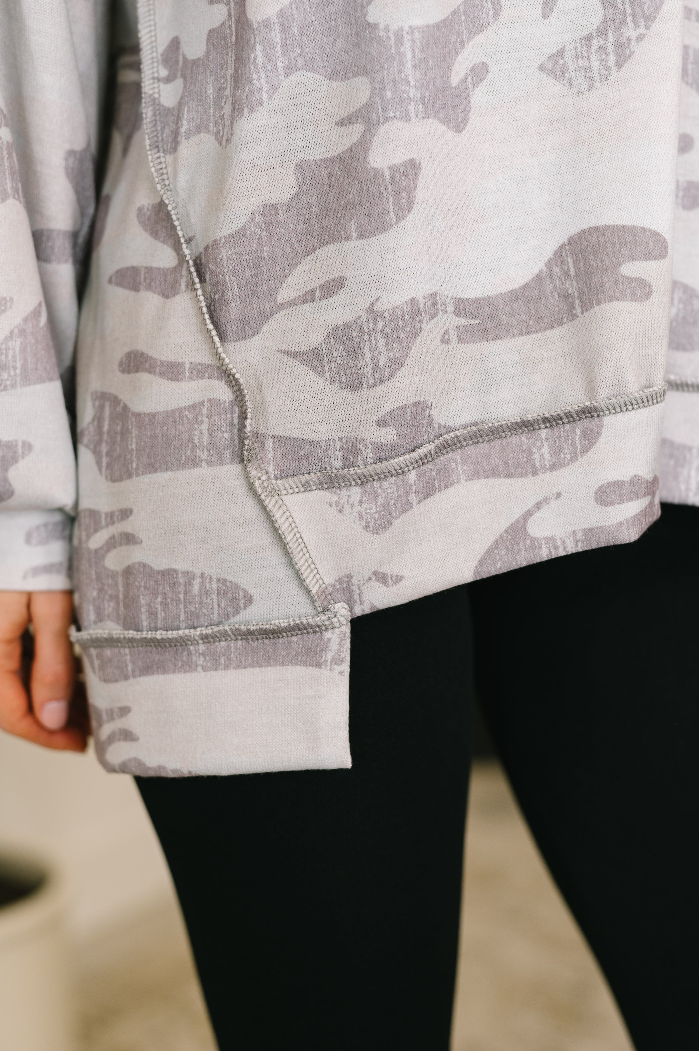 Close-up of grey camo drop shoulder top with raw seam detailing paired with black leggings on model indoors