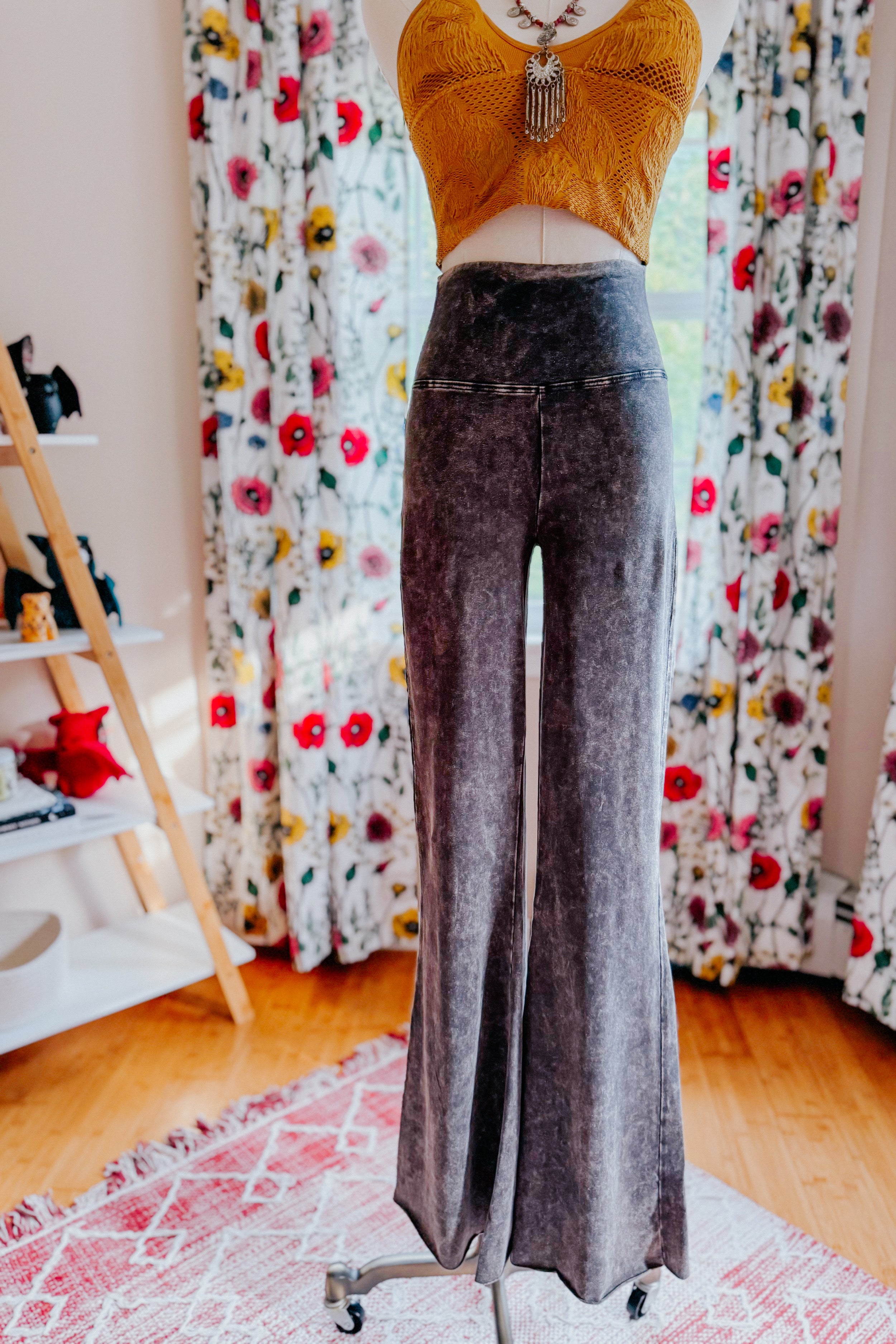 Mannequin wearing ash black acid wash flare pants paired with a mustard crochet crop top and pendant necklace indoors