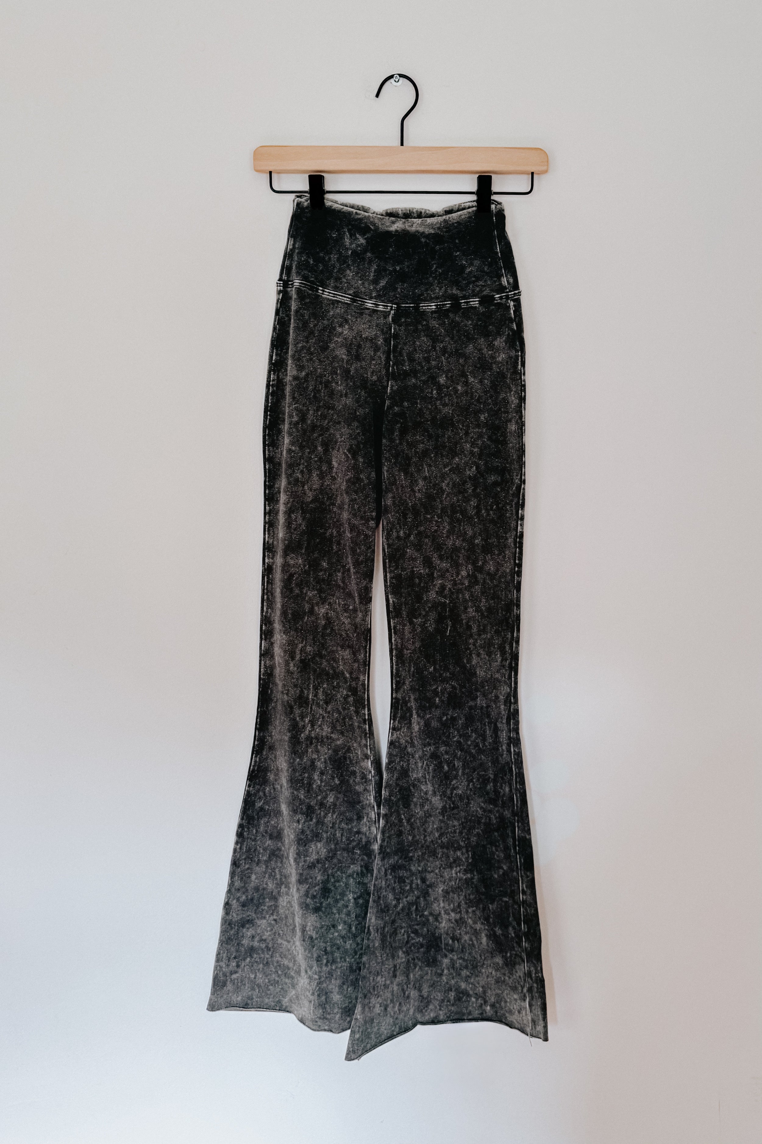 Ash black acid wash flare pants hanging on wooden hanger against white wall