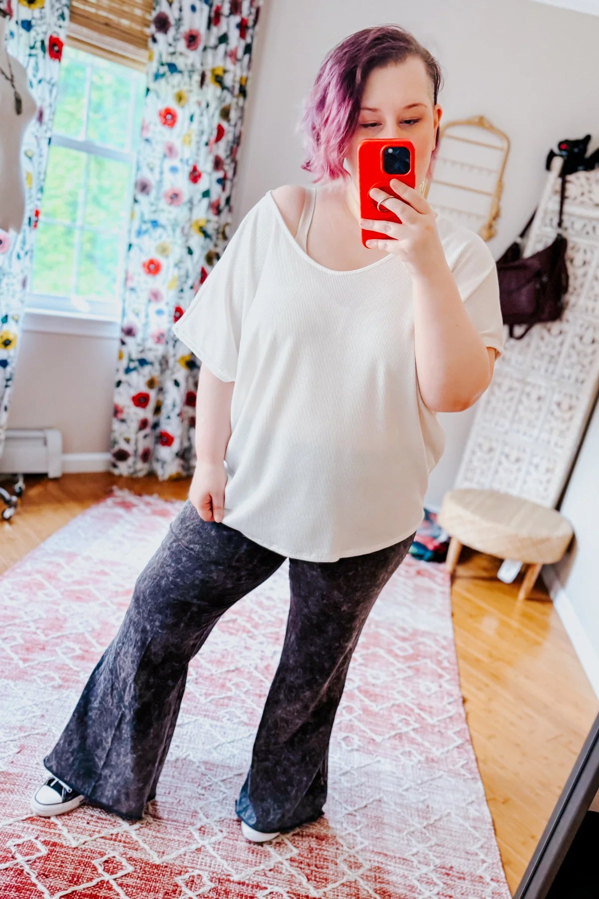 Plus-size model wearing ash black acid wash flare pants paired with a loose white top indoors in a bright room