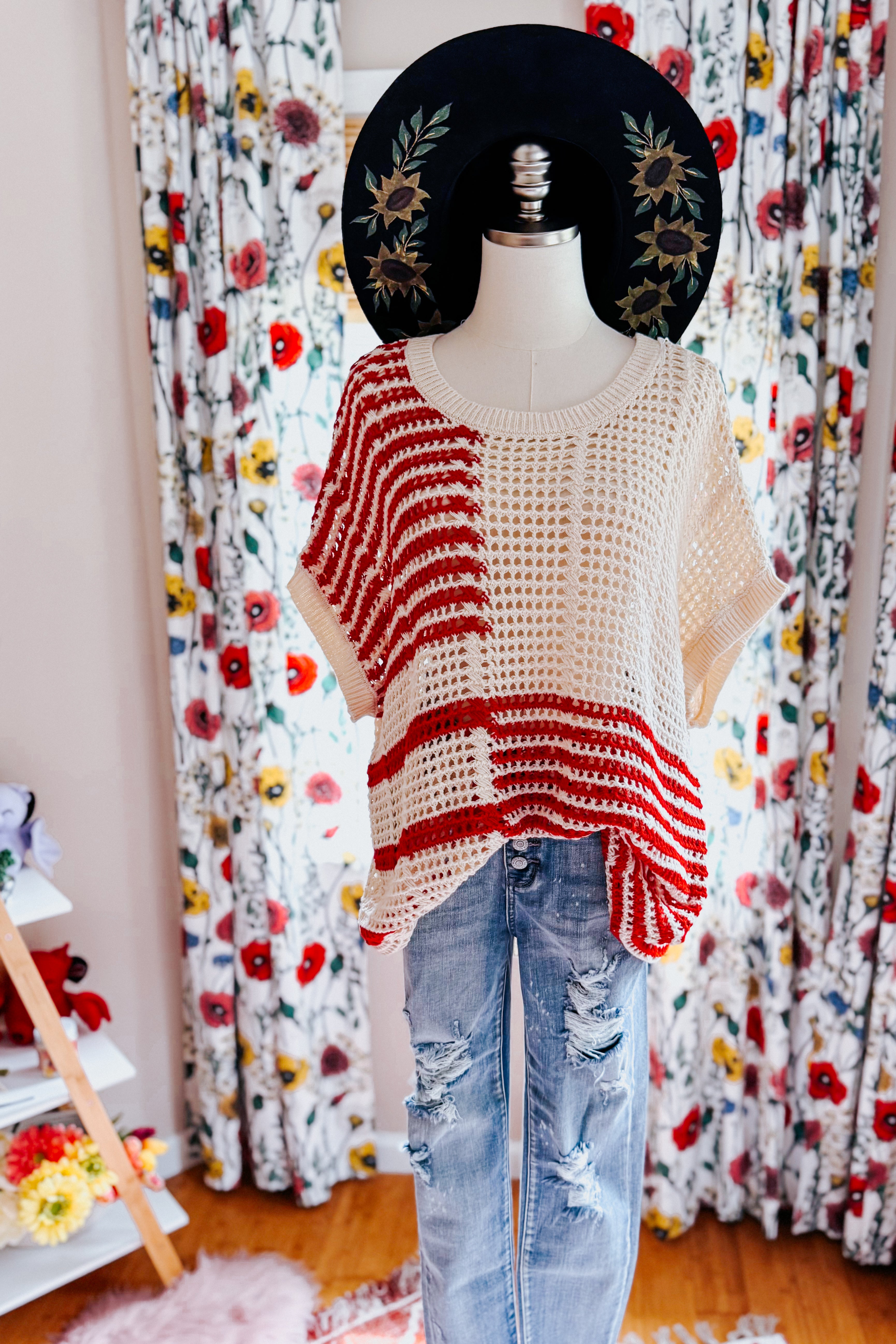 Mannequin wearing red striped open-knit top paired with distressed blue jeans and black floral embroidered hat indoors