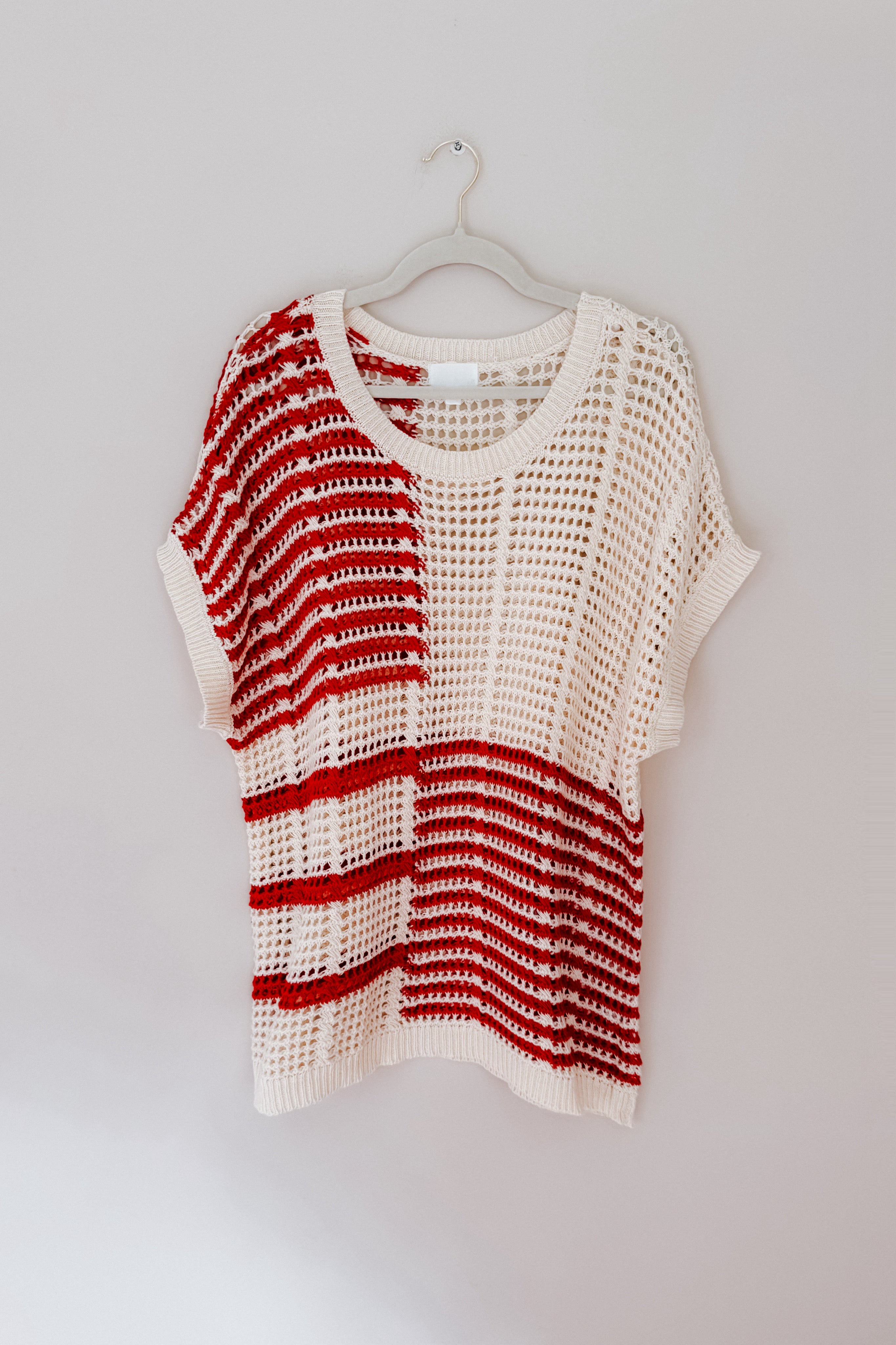 Chunky knit net top with bold red stripes and open weave design hanging on beige wall hook