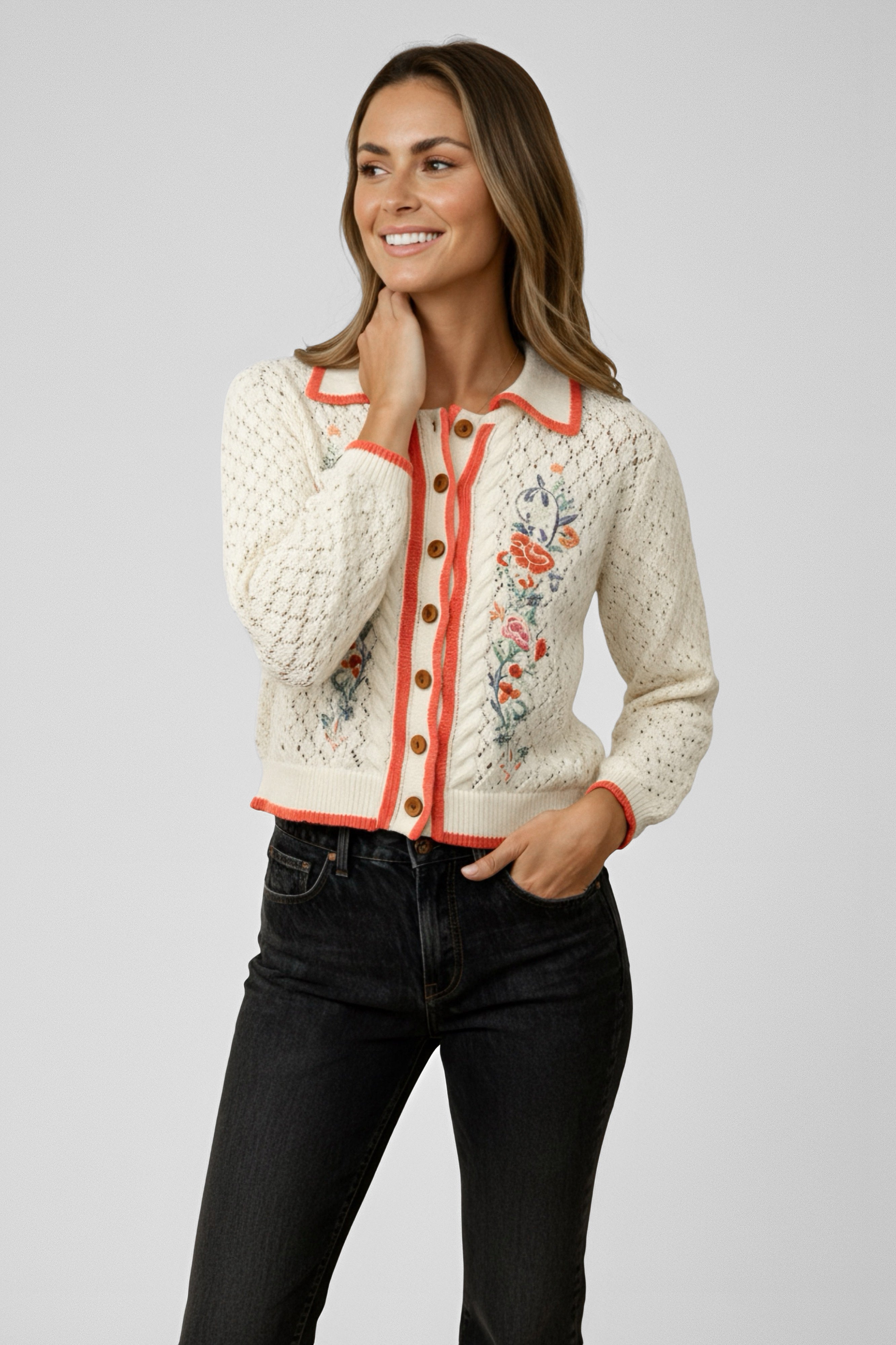 Woman wearing a cream knit cardigan with orange trim, floral embroidery, and wooden buttons paired with black jeans