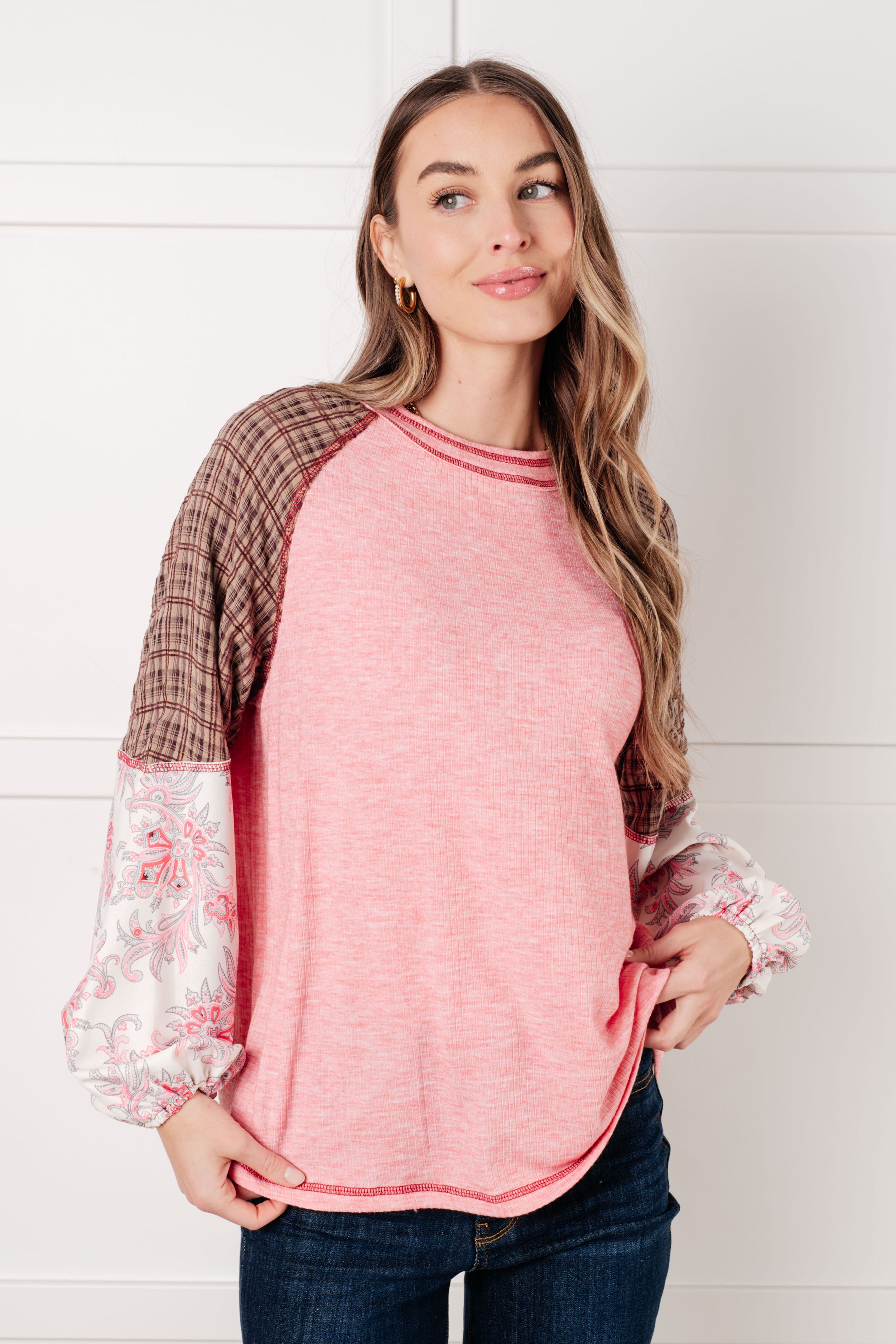 Woman wearing pink color block top with brown plaid upper sleeves and floral puffed lower sleeves standing with hand in pocket