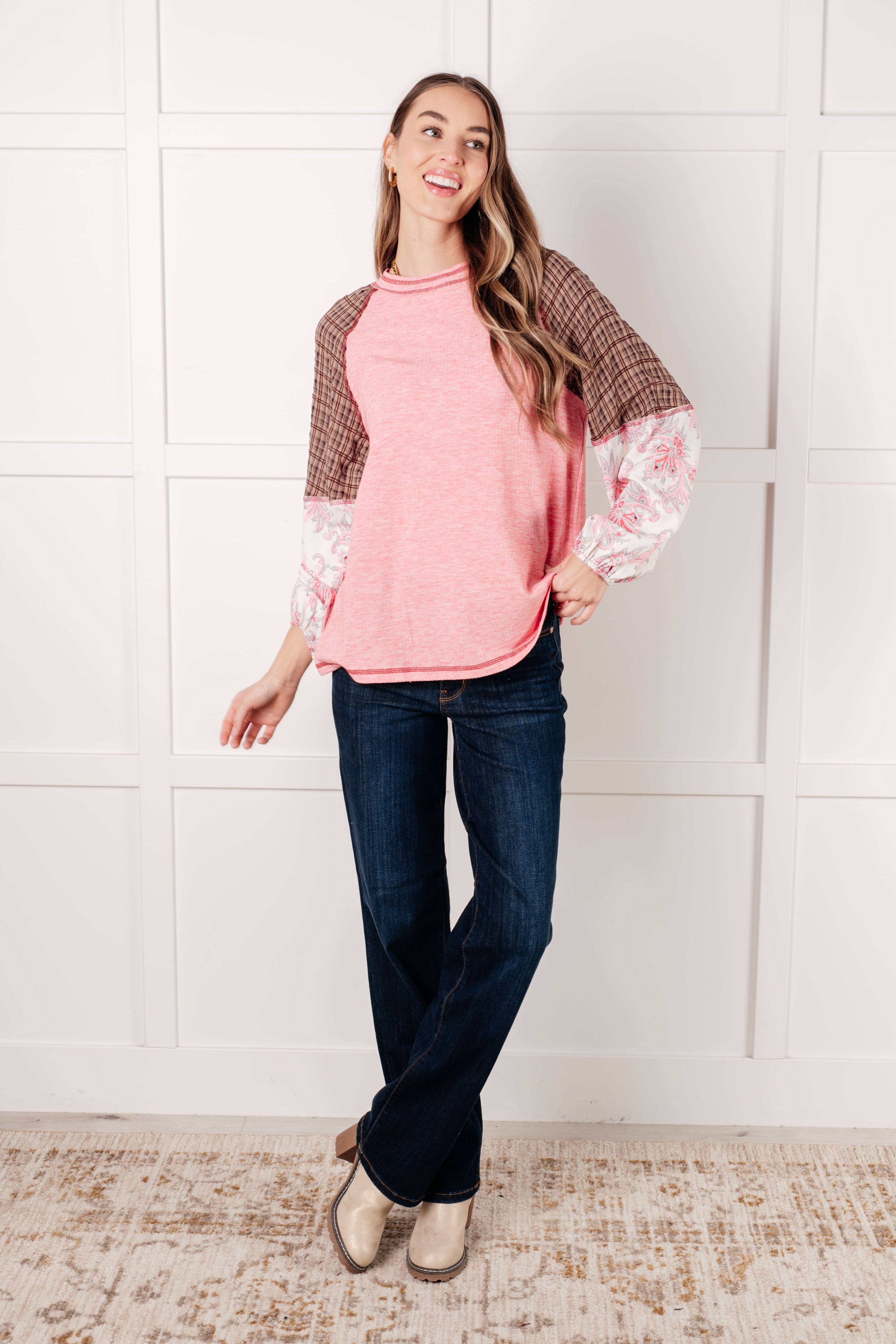 Woman wearing pink floral color block top with brown plaid and floral sleeves paired with dark blue jeans and beige boots