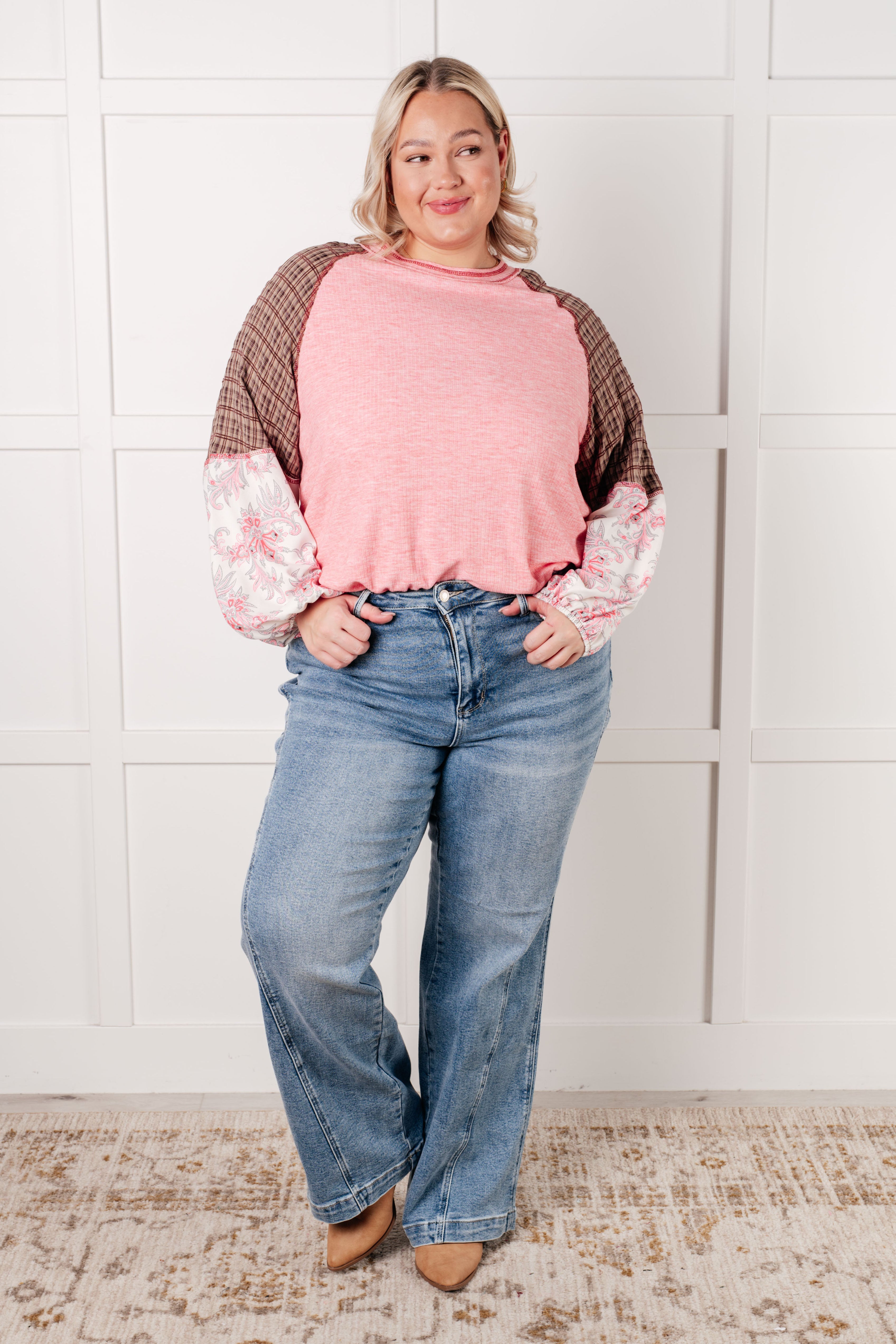 Plus size model wearing pink top with brown plaid upper sleeves and floral puffed lower sleeves paired with blue jeans