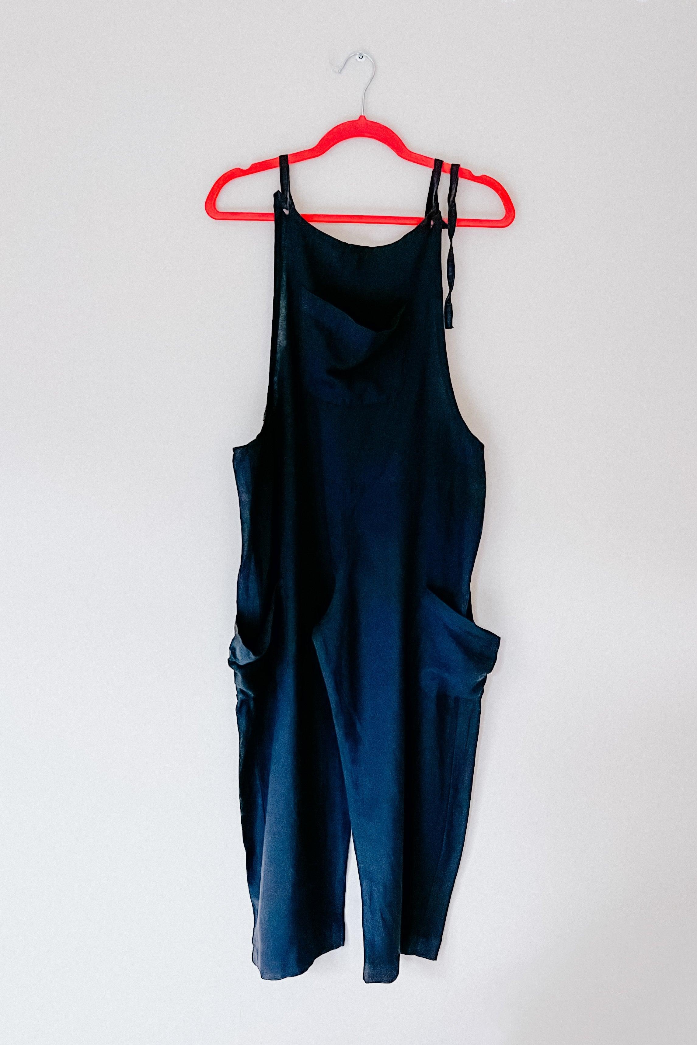 Black slouchy hemp viscose overalls hanging on red hanger against plain light wall background