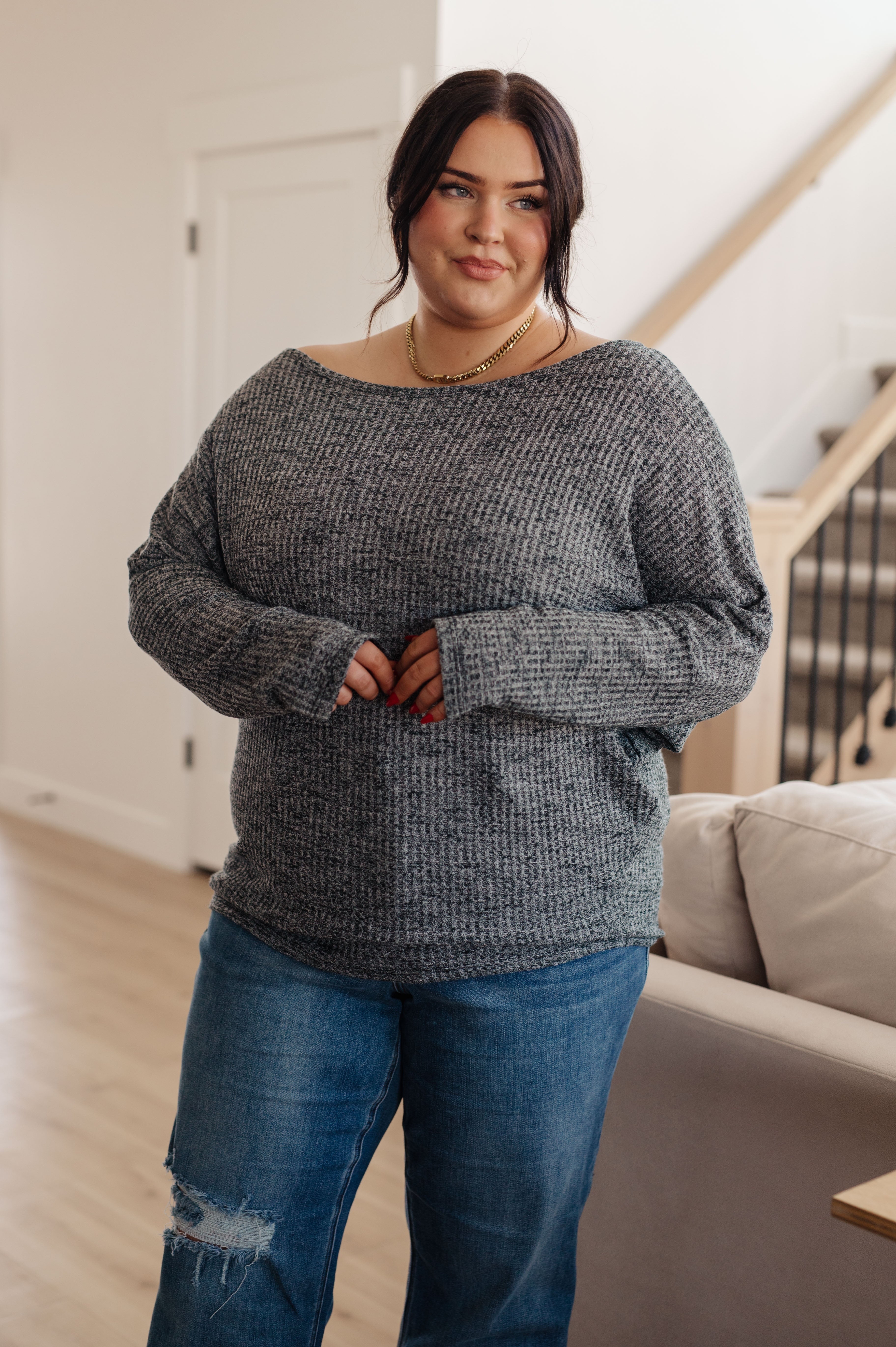 Woman wearing charcoal ribbed sweater with relaxed fit paired with distressed blue jeans indoors in cozy setting