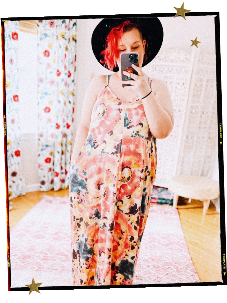 Woman with pink hair in a pink tie dye maxi dress wearing a wide brim hat and scattered gold star decals