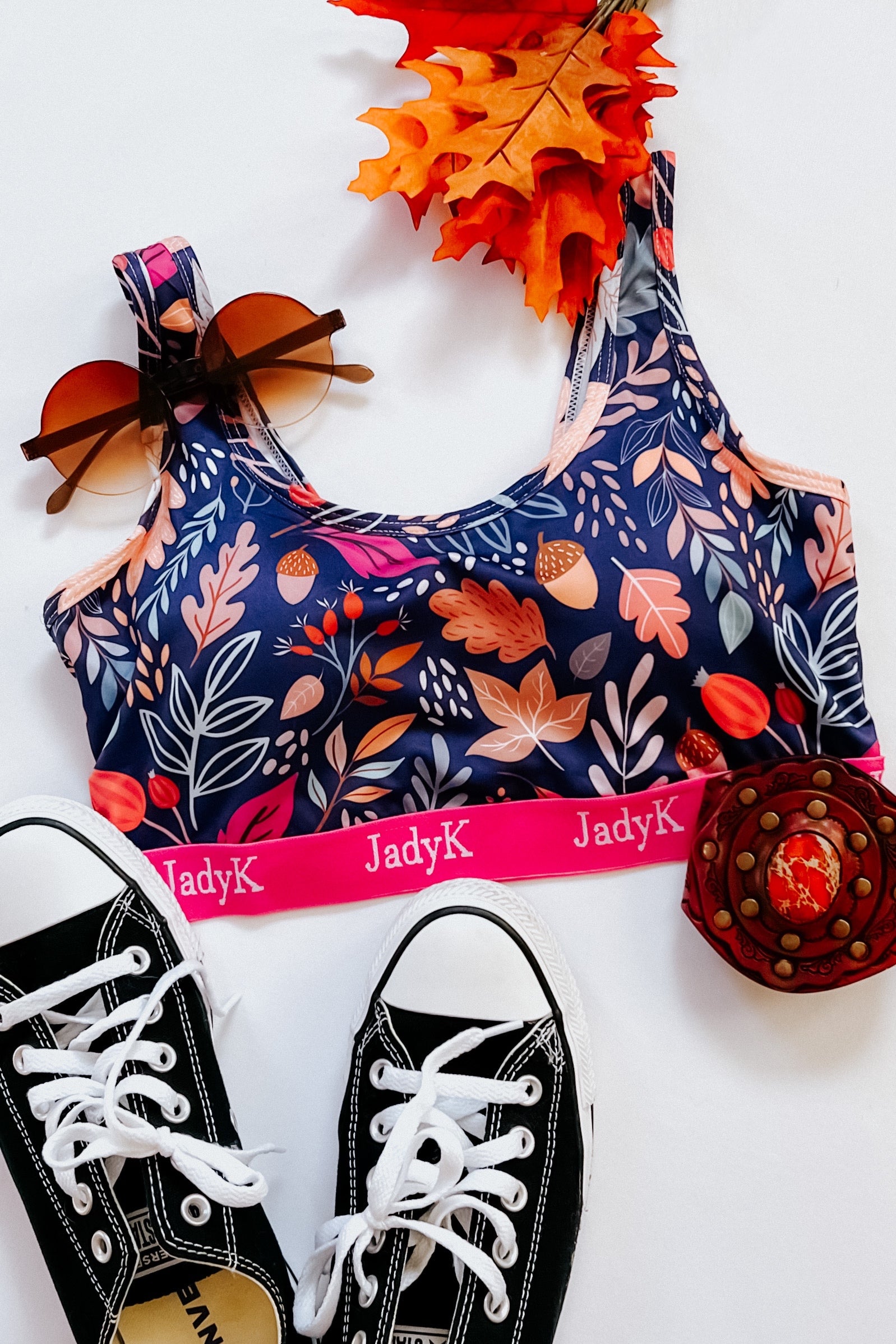 Blue bralette with fall leaf print and pink band styled with black sneakers, sunglasses, and autumn leaves accessory
