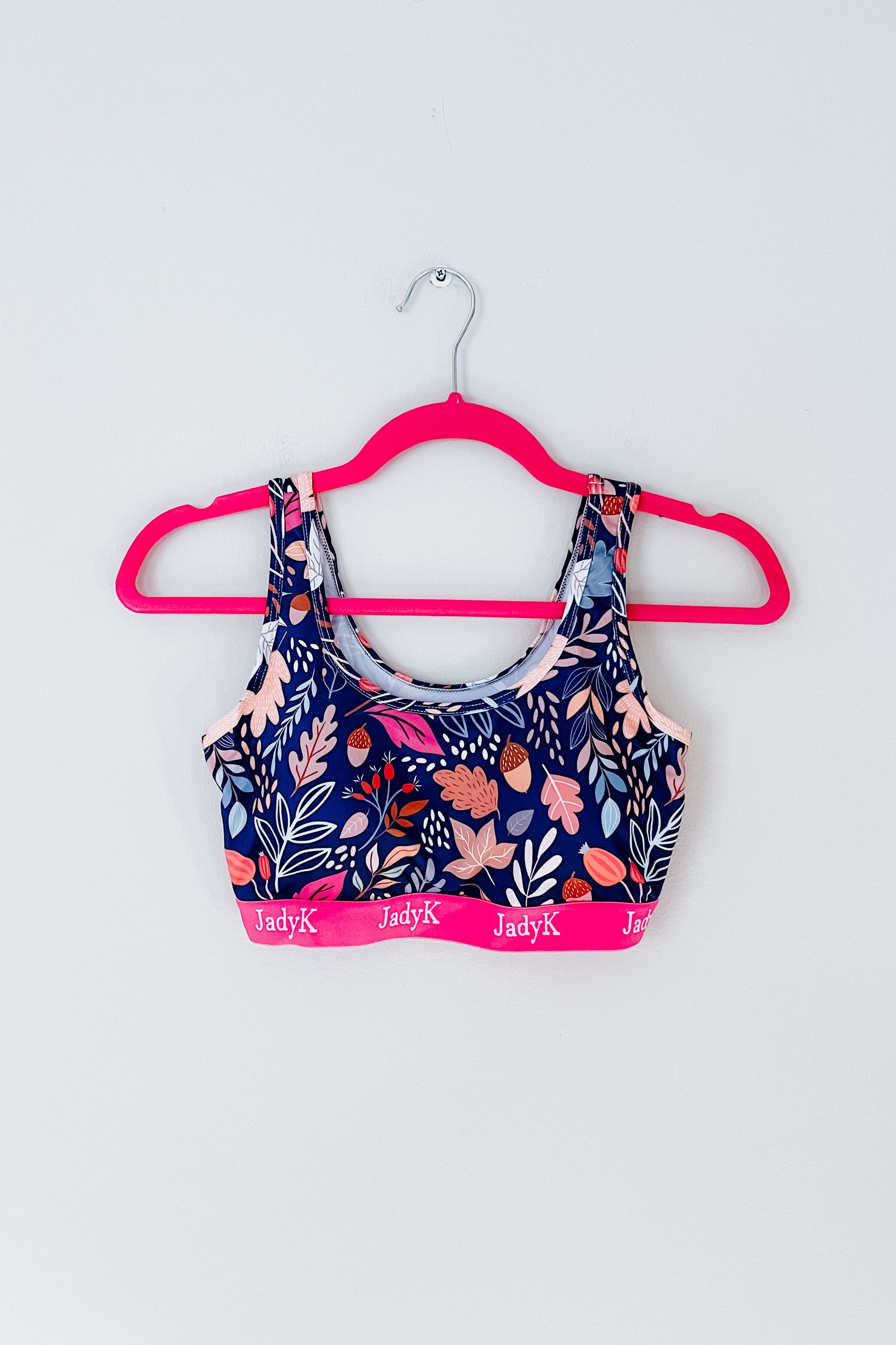 Blue floral sports bra with pink band on bright pink hanger against white background