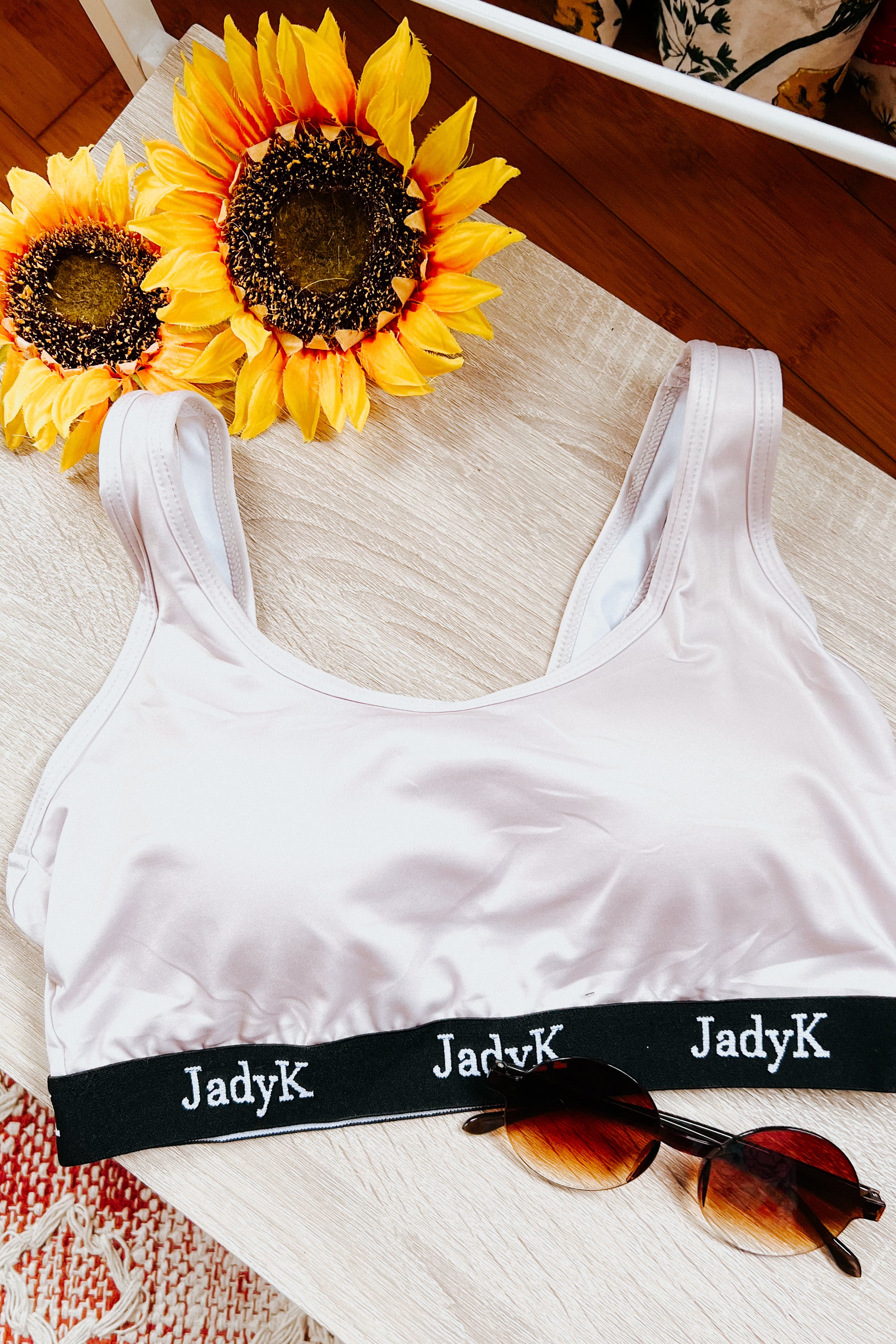 Champagne-colored bralette with black JadyK band styled with tortoiseshell sunglasses and sunflowers on light wood surface