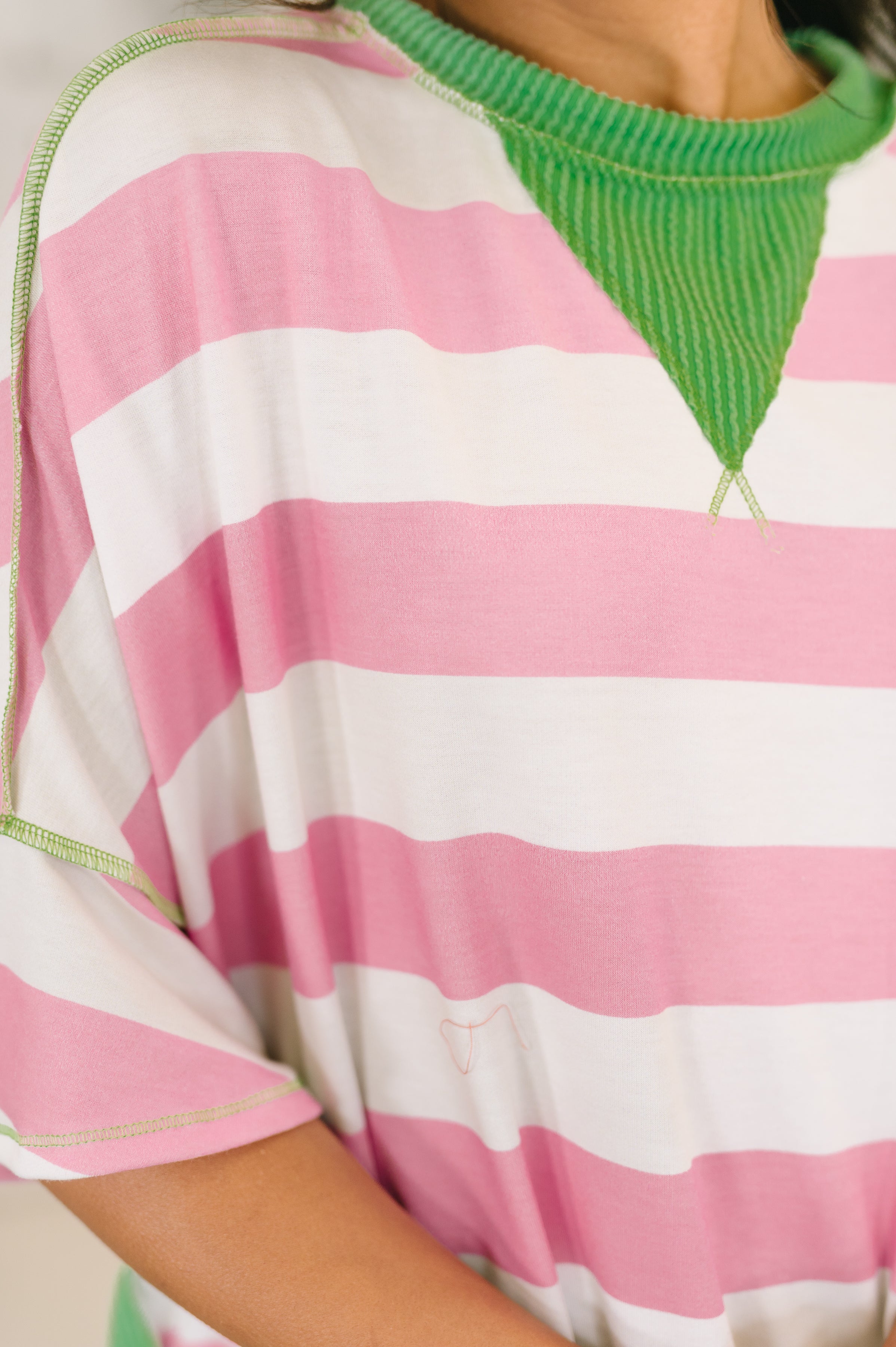Close-up of pink and white striped relaxed top with contrast green ribbed trim and stitching on neckline and sleeves