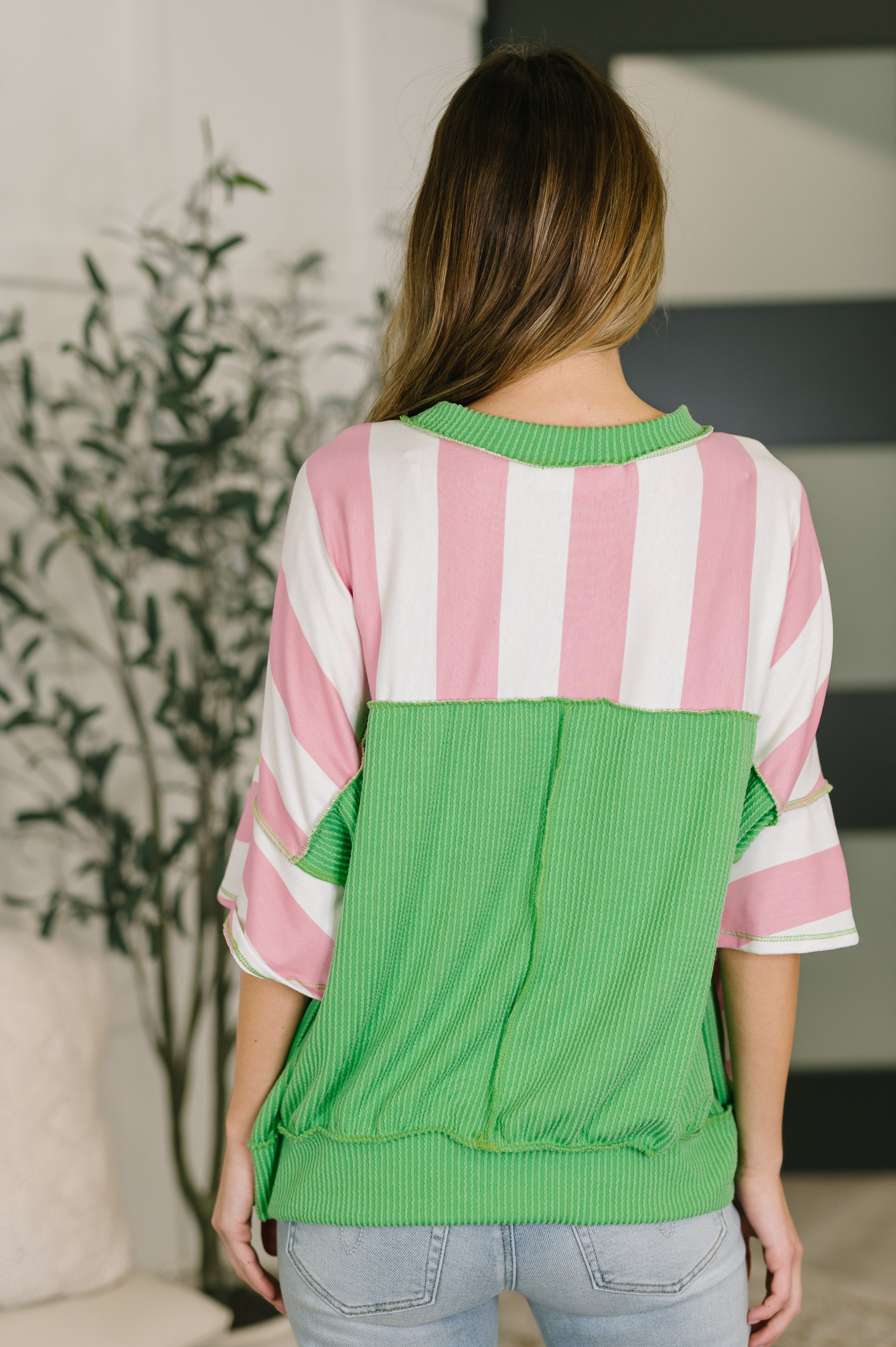 Back view of relaxed pink and white striped top with bright green ribbed contrast trim and wide sleeves indoors