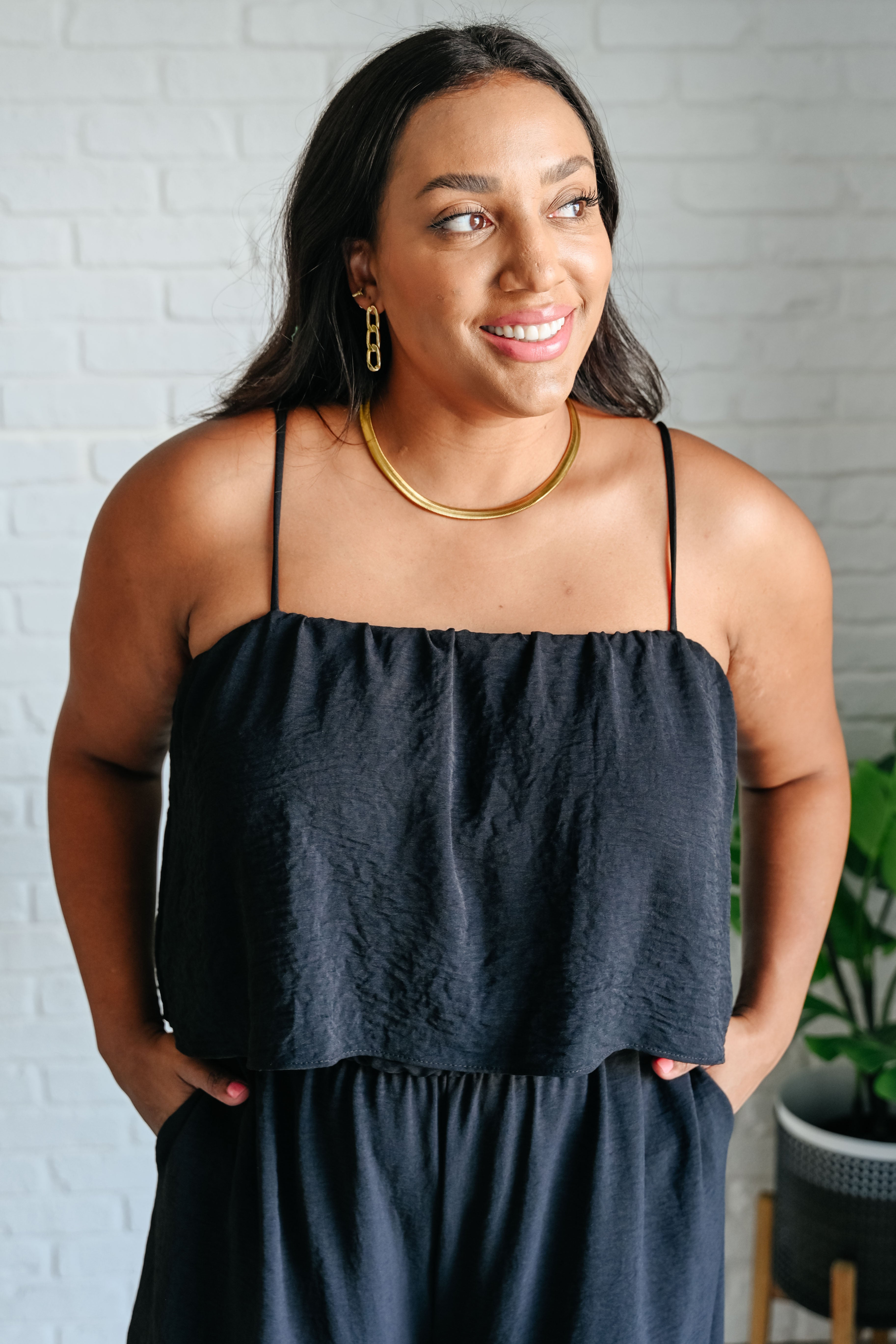 Smiling woman wearing a black sleeveless top with thin straps and matching black bottoms indoors