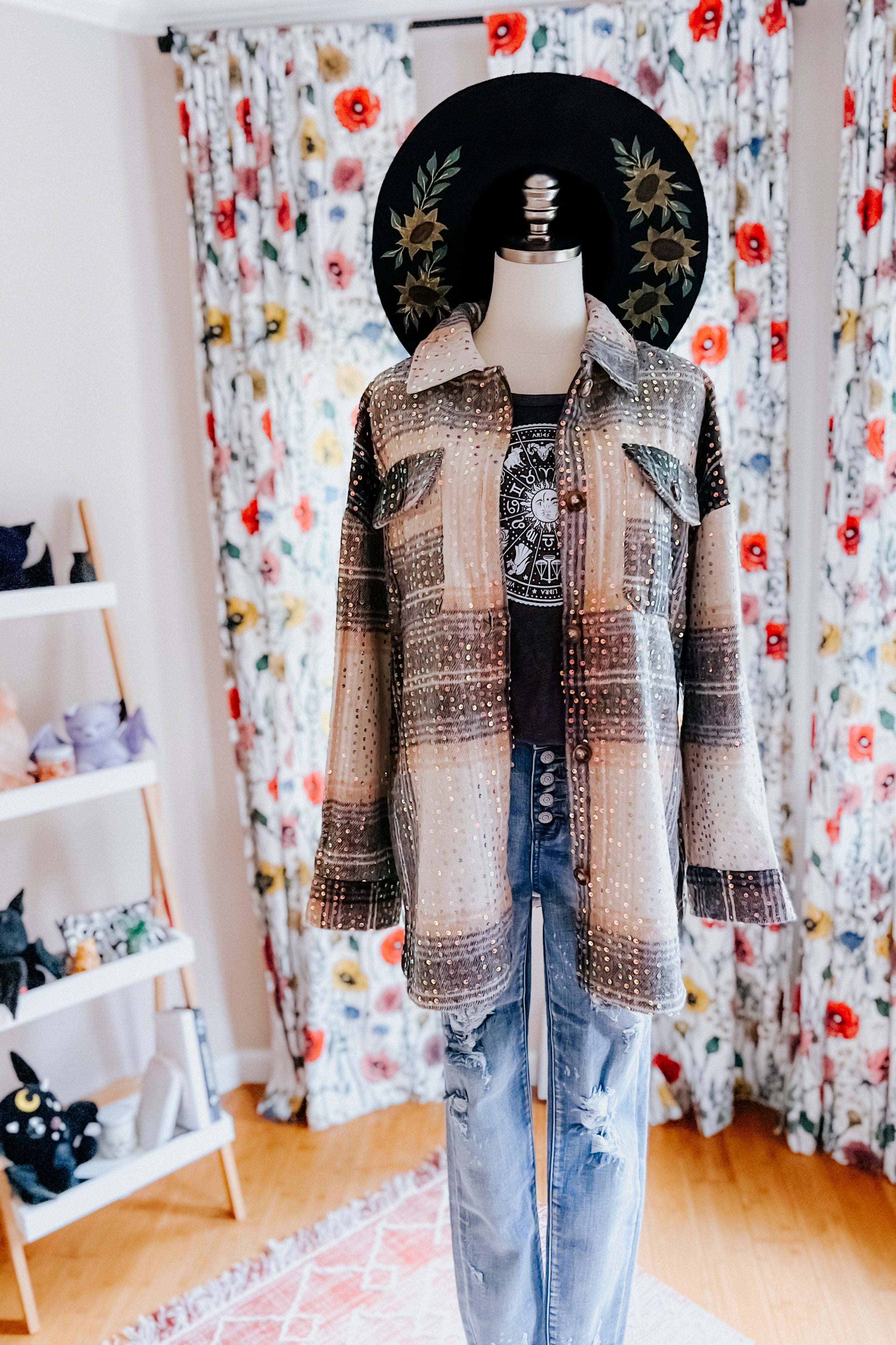 Beige and black sequin plaid shacket layered over graphic tee and distressed jeans on mannequin with black floral hat