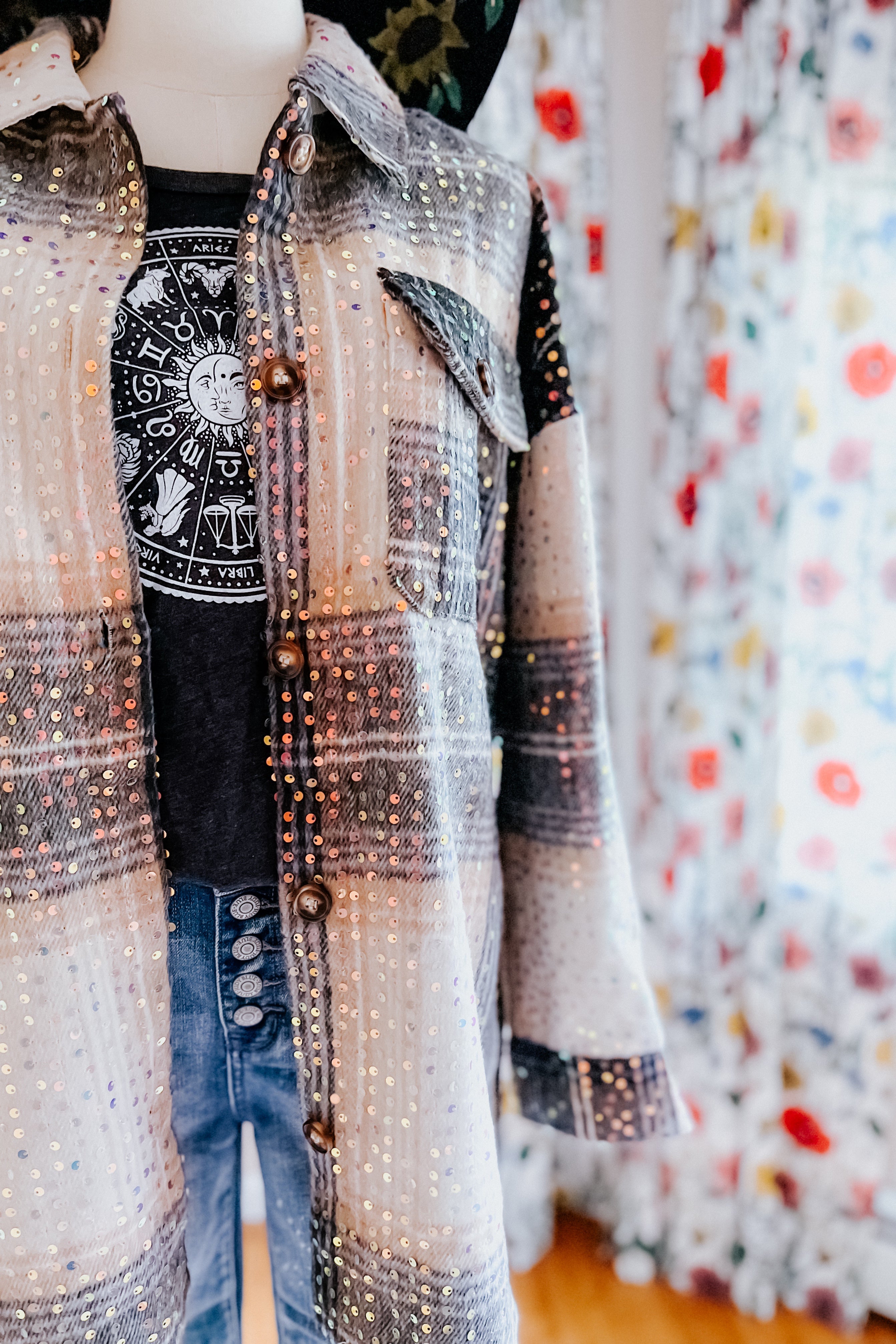 Beige and black plaid shacket with sequins layered over zodiac print black tee and high-rise jeans on mannequin indoors