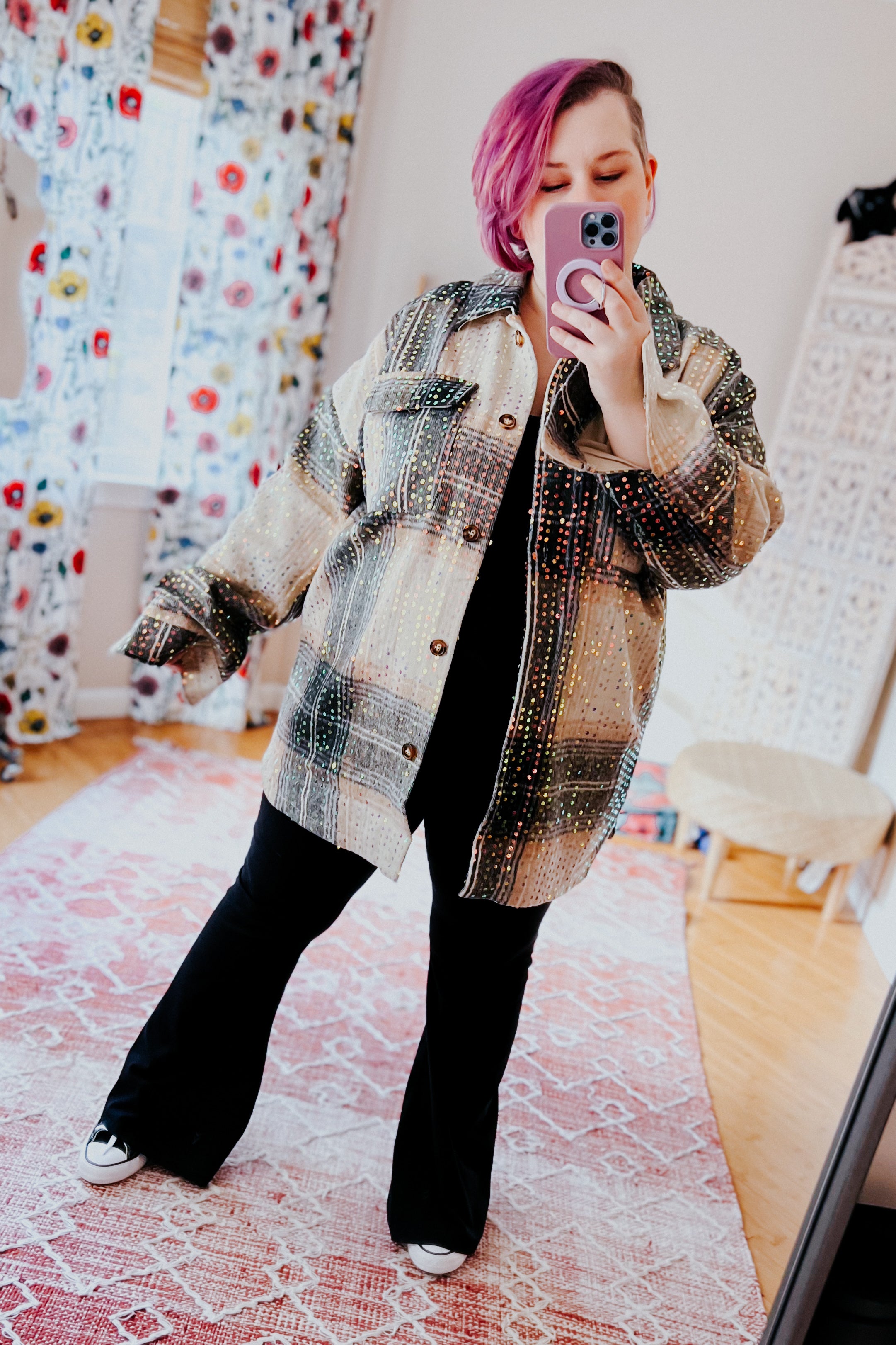 Woman with vibrant pink hair wearing beige and black sequin plaid shacket over black outfit, taking a mirror selfie indoors