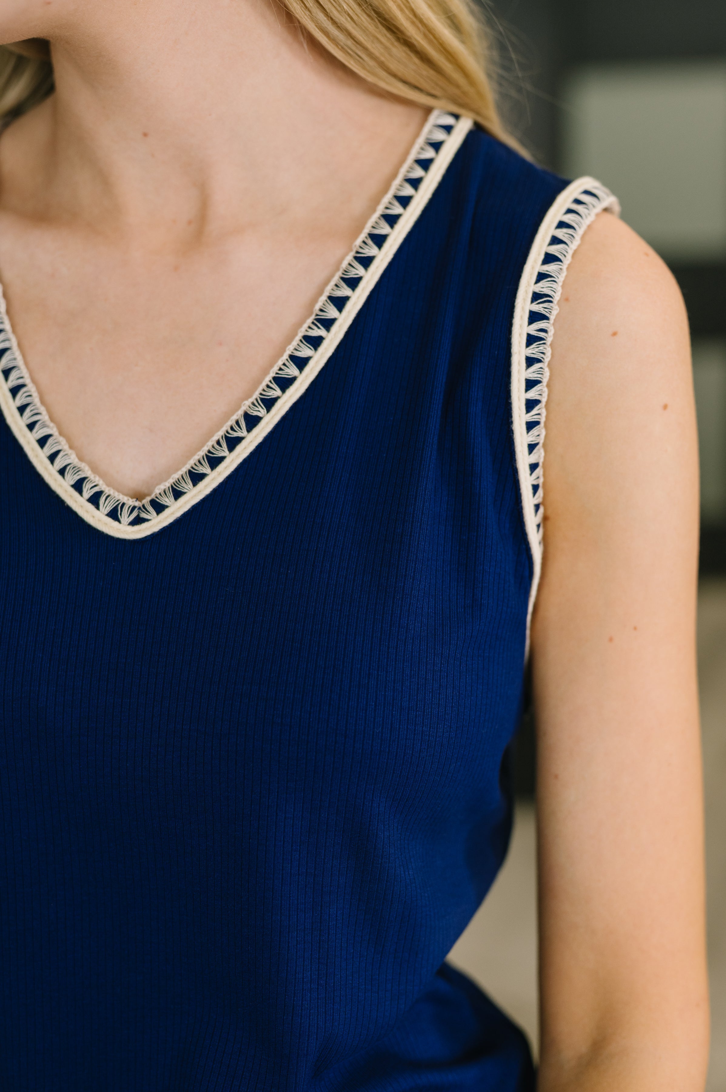 Close-up of navy sleeveless tank with V-neck and white lace trim on neckline and armholes worn by woman
