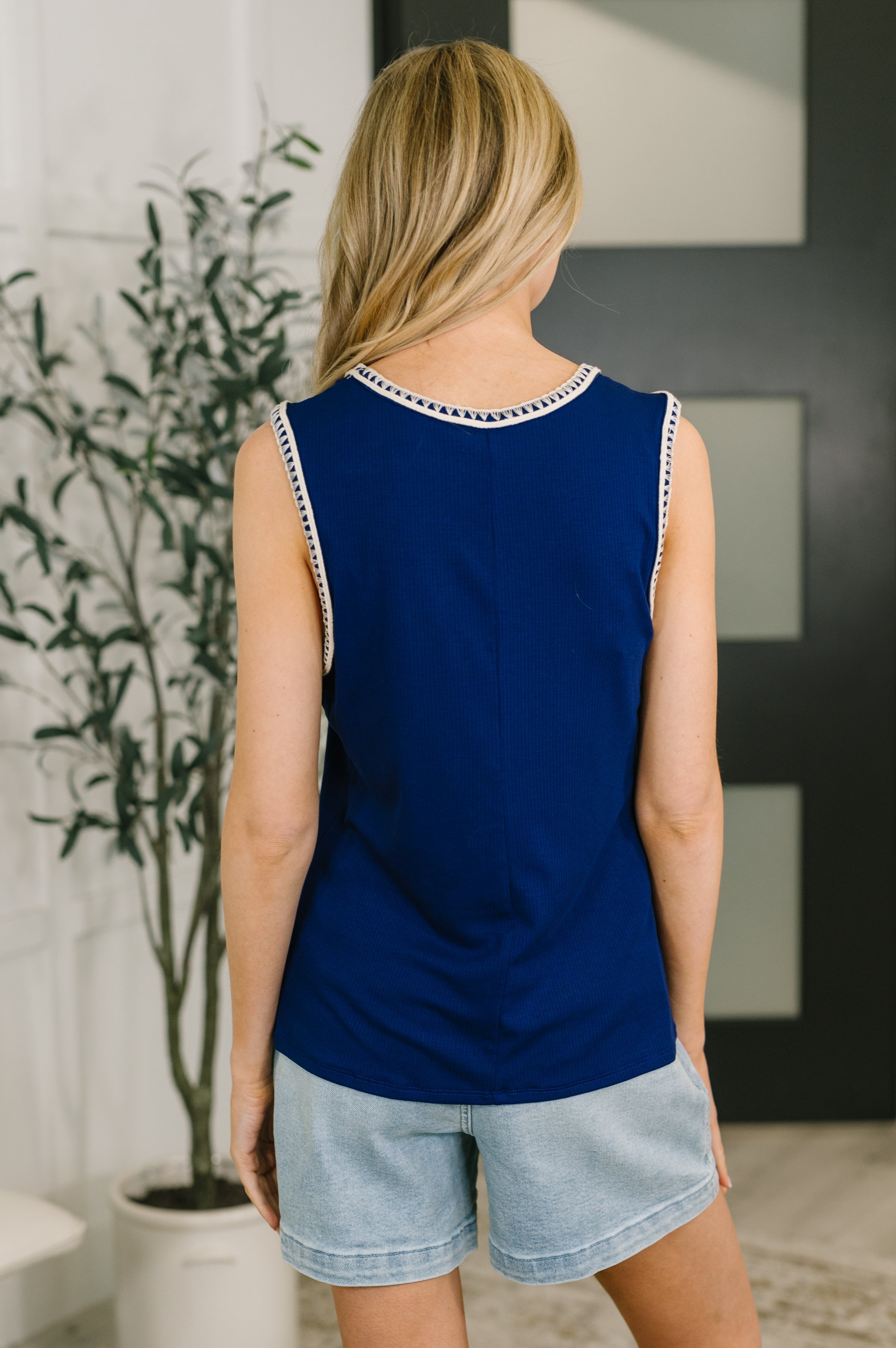 Woman wearing navy sleeveless tank with subtle trim detail paired with light denim shorts standing indoors