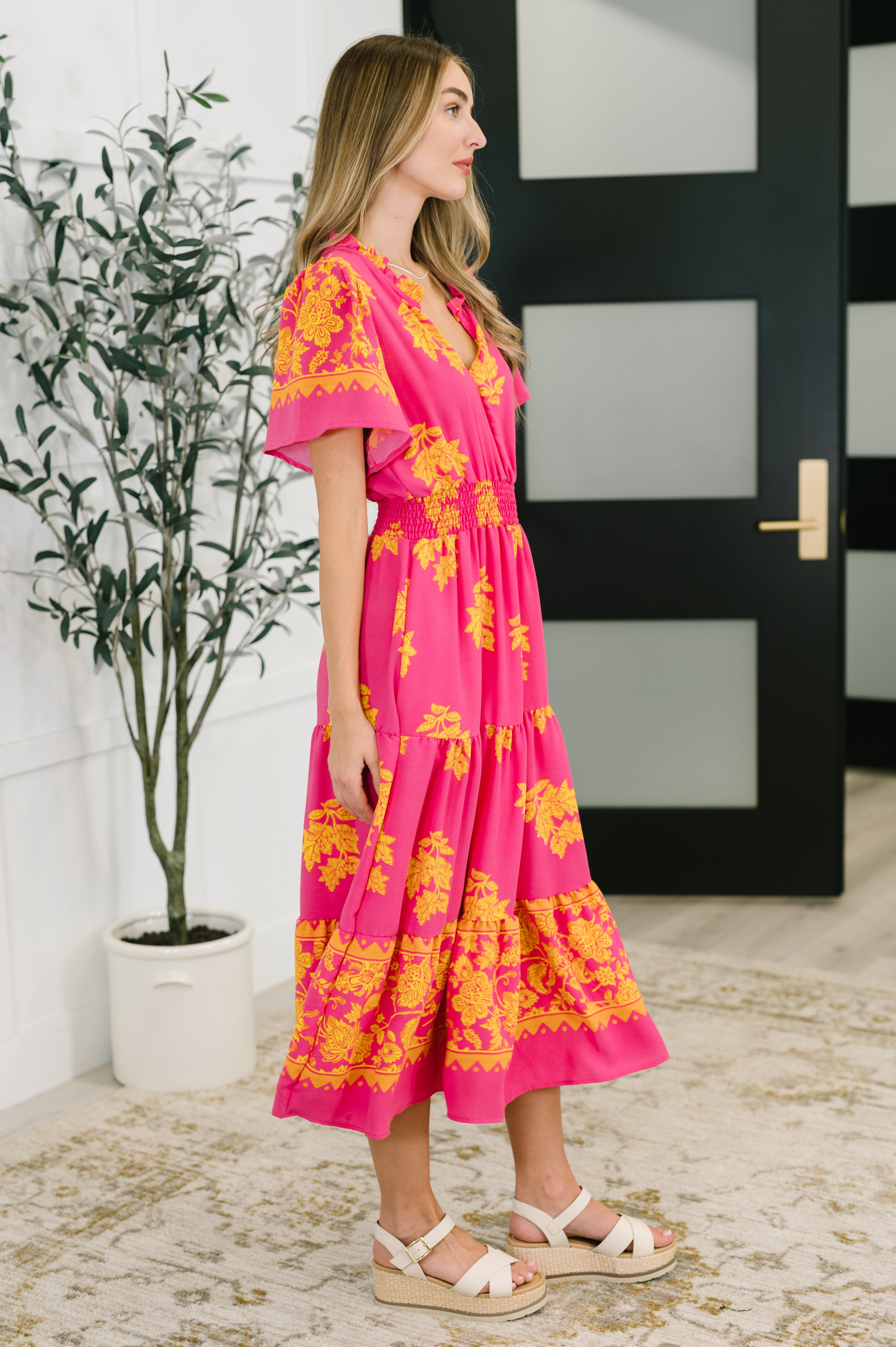Side profile of woman wearing fuchsia V-neck dress with yellow floral pattern and flutter sleeves indoors