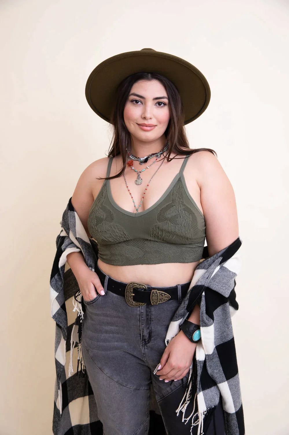 Woman wearing olive seamless padded brami top with layered necklaces, hat, and patterned shawl indoors