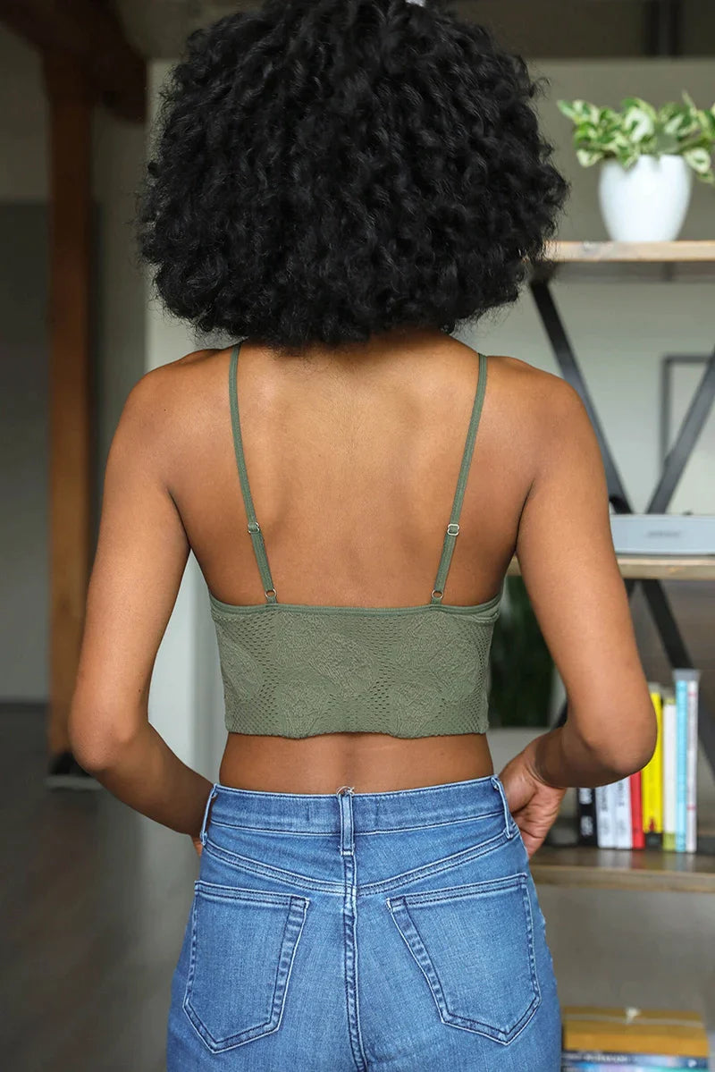 Woman wearing olive textured brami top with thin straps paired with blue jeans standing indoors near bookshelf