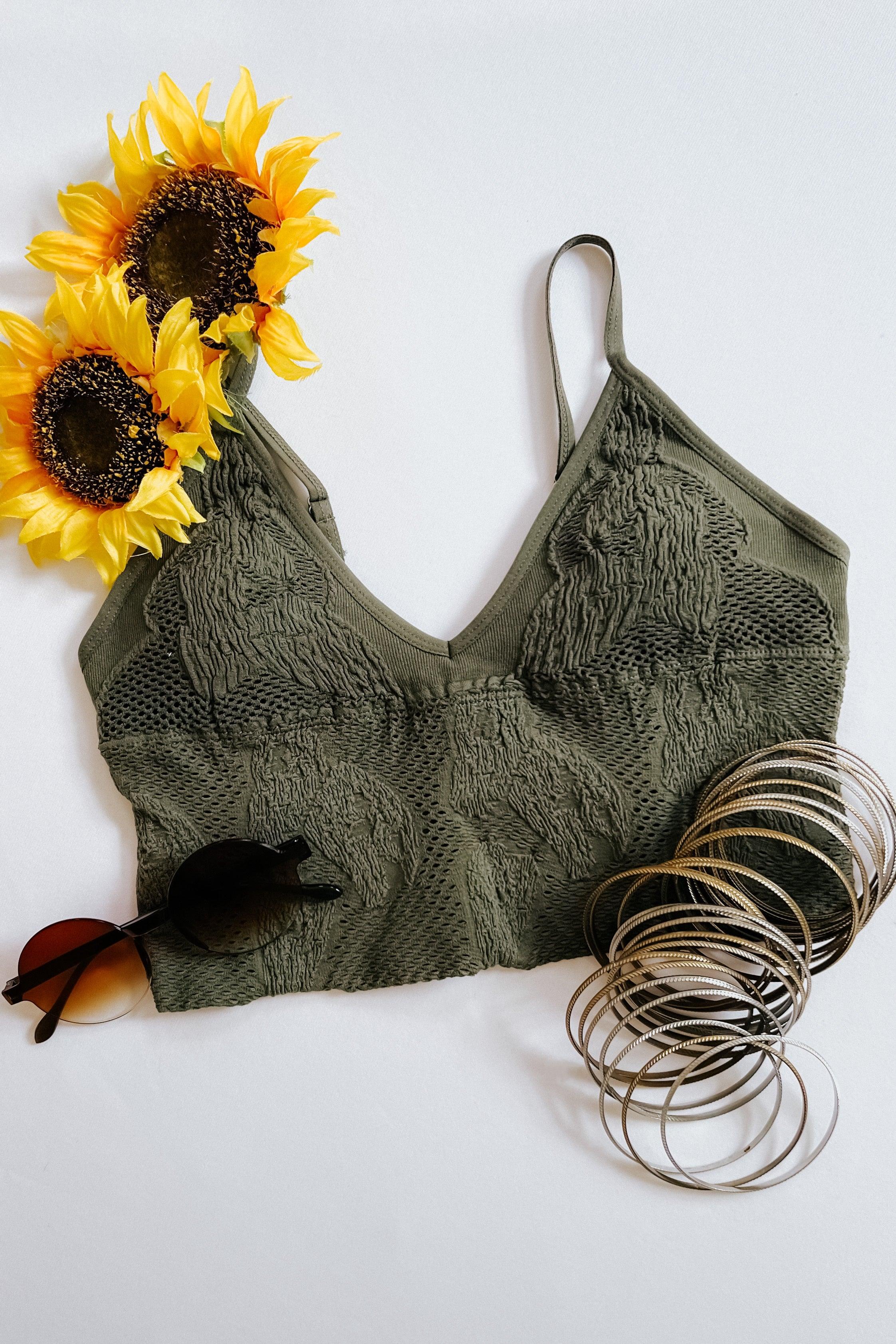 Olive textured seamless padded brami styled with bright sunflowers, round sunglasses, and a stack of silver bangles on white background