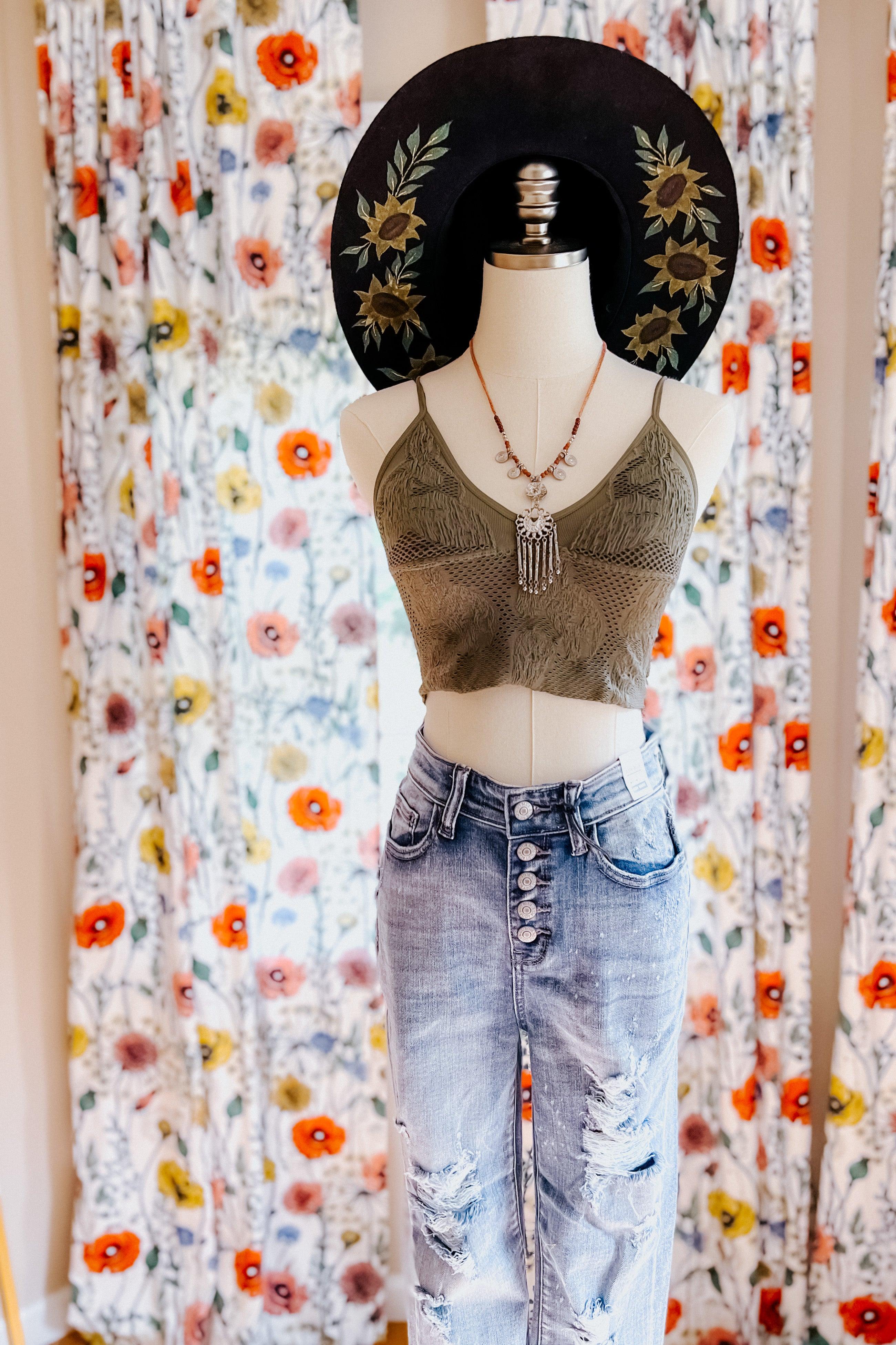 Mannequin dressed in olive textured brami with layered necklaces, distressed jeans, and wide-brim sun hat with floral accents
