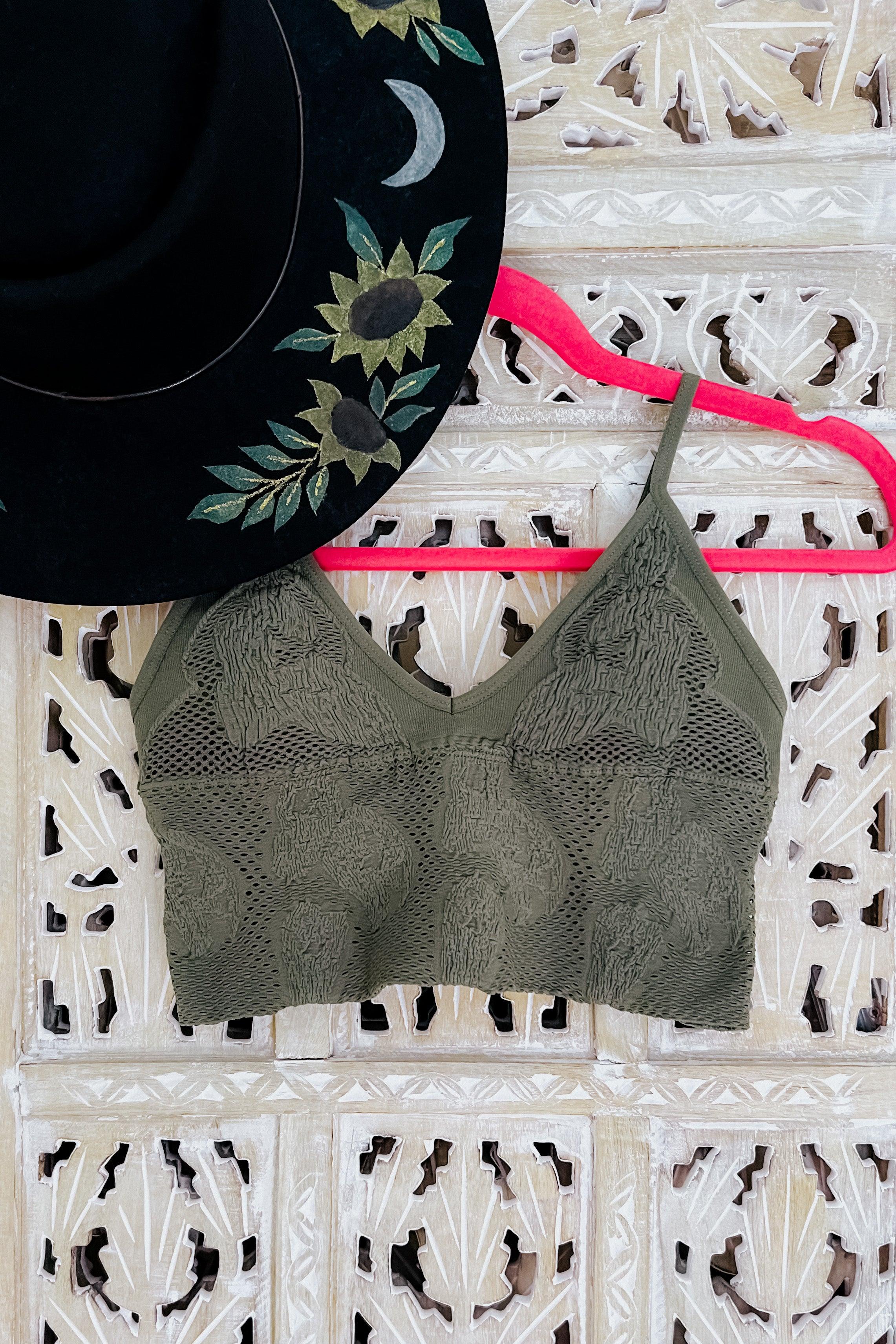 Olive textured brami top with seamless design hanging on bright pink hanger against carved wood background