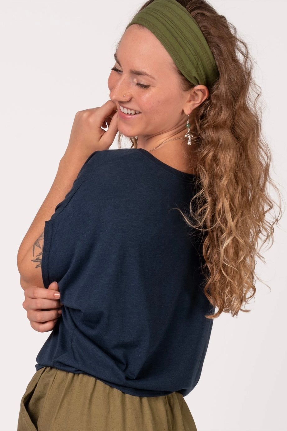 Woman with curly hair wearing navy bamboo dolman top and olive headband smiling with eyes closed against white background
