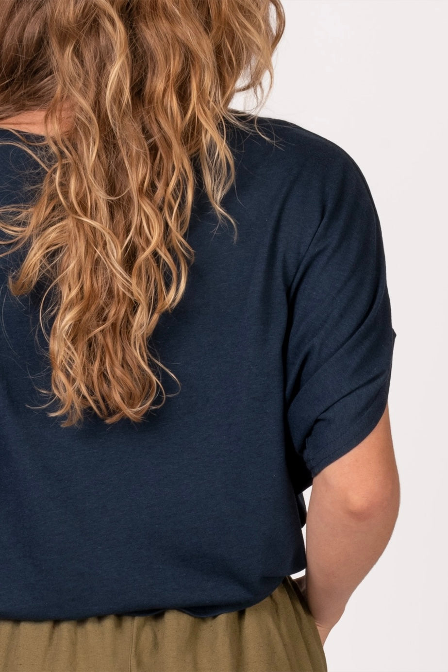 Woman with wavy blonde hair wearing navy bamboo dolman top with rolled sleeves and olive pants against light background