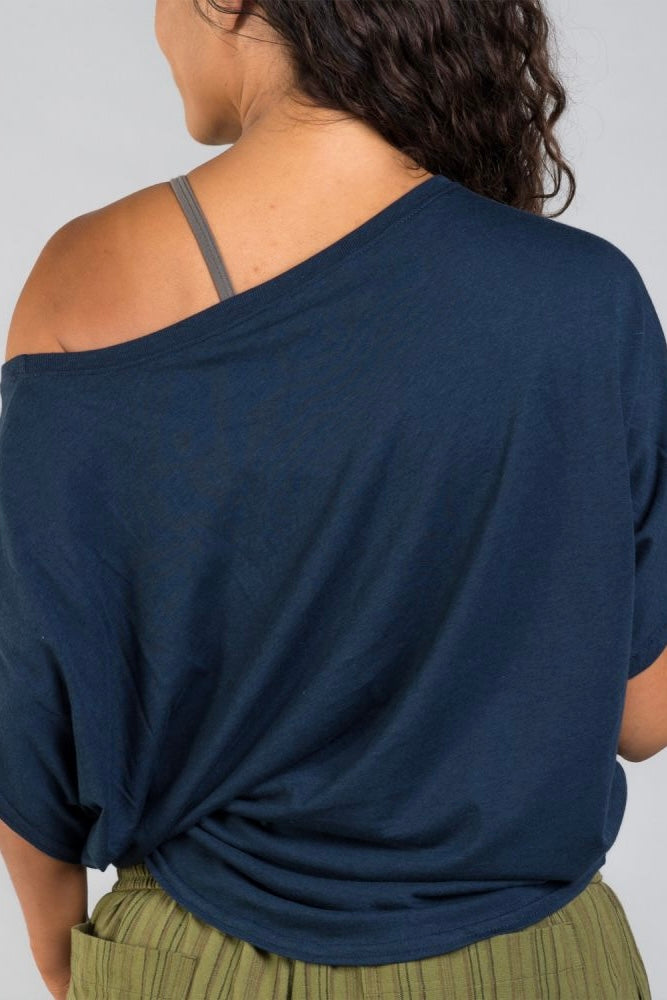 Back view of person wearing navy bamboo dolman top slightly off shoulder with olive pants and gray strap visible