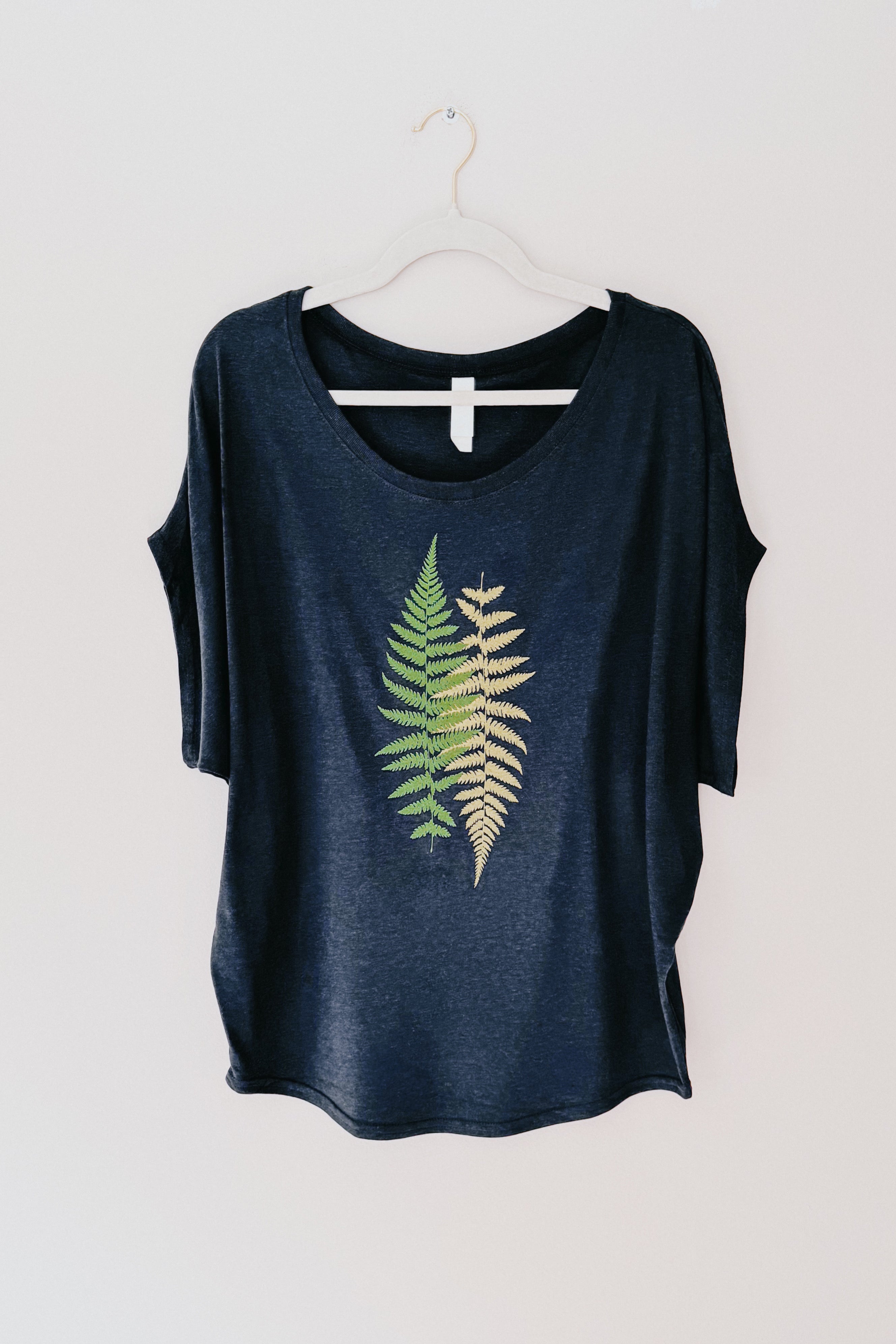 Navy bamboo dolman top with green and beige fern graphic hanging on white hanger against plain background