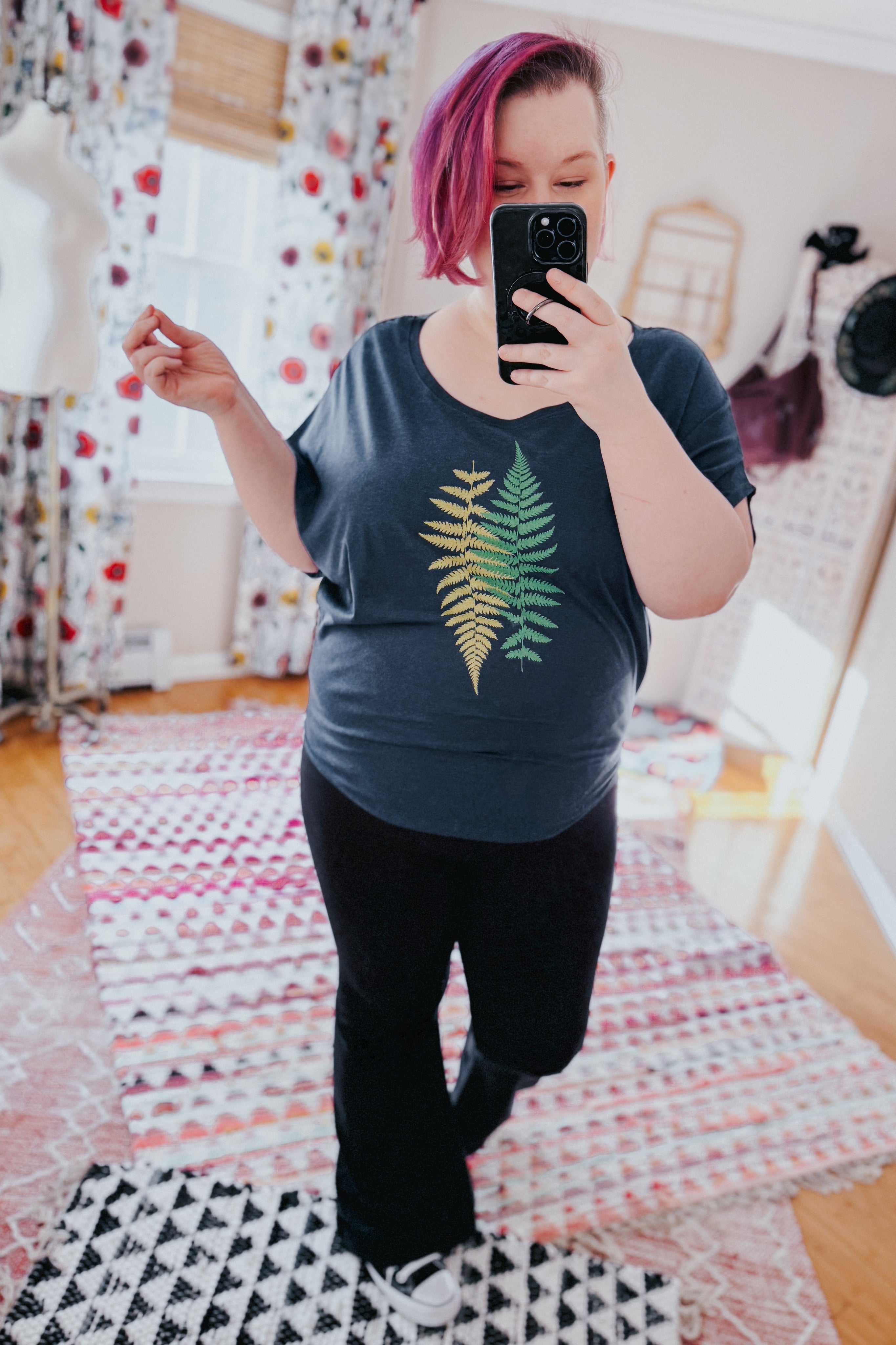 Woman with pink hair wearing navy bamboo dolman top featuring fern print, black pants, taking indoor mirror selfie